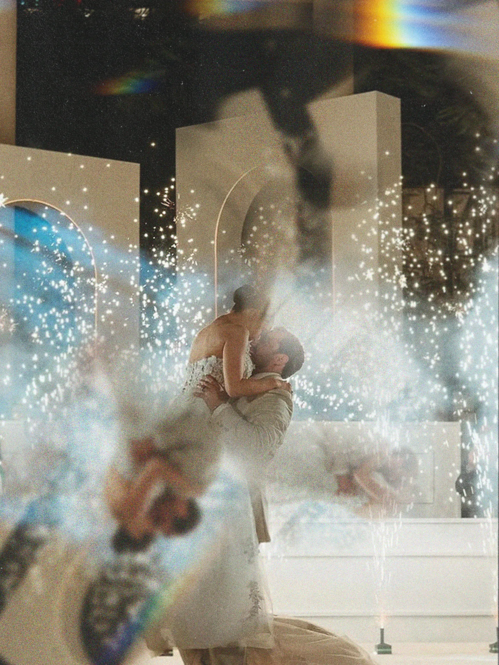 Una pareja se besa apasionadamente entre brillantes fuegos artificiales en una fiesta al aire libre. La atmósfera evoca alegría y celebración, creando un ambiente mágico.