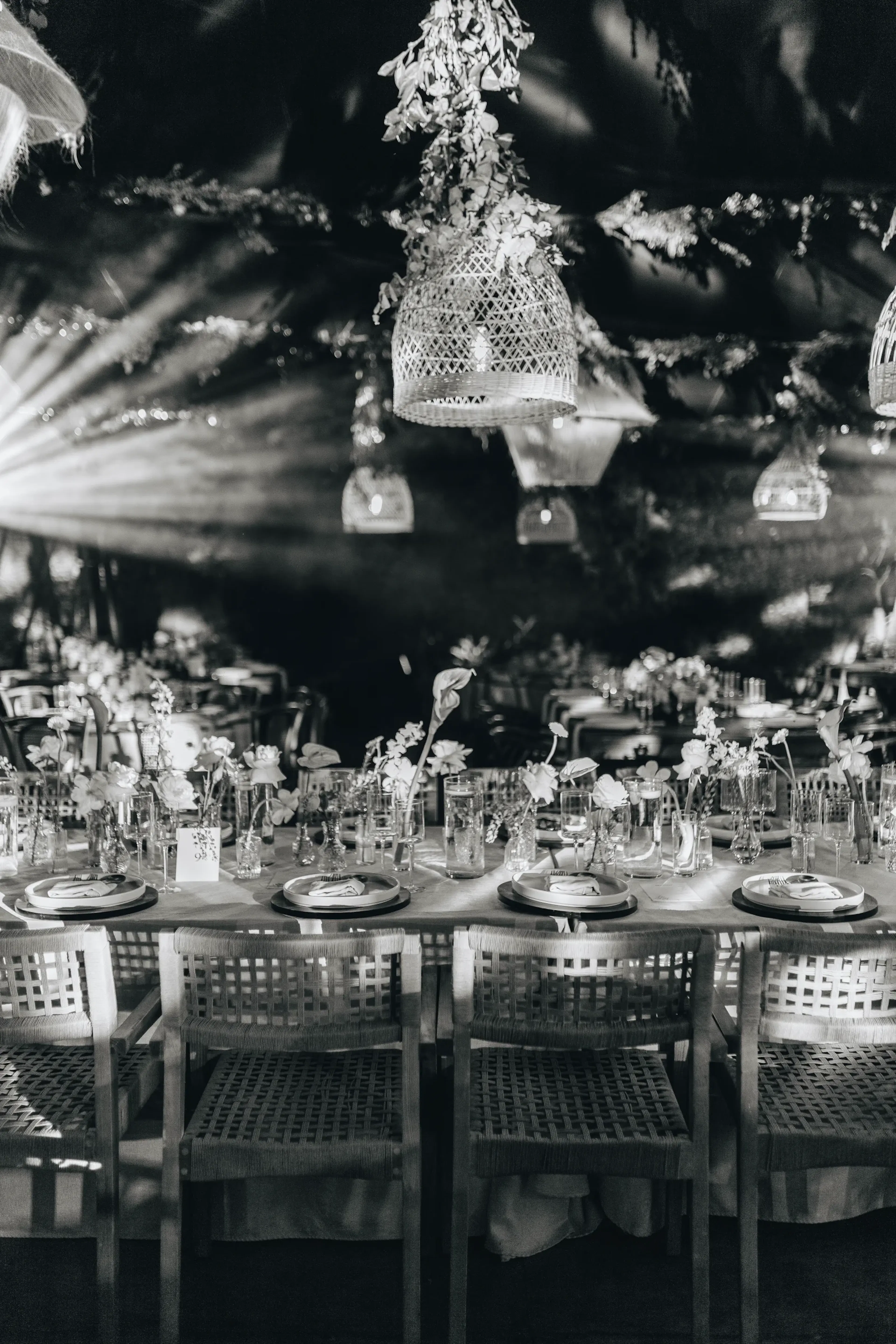Elegante recepción de boda en blanco y negro con sillas tejidas, centros de mesa florales e iluminación suave de lámparas tejidas en el techo, creando un ambiente romántico.
