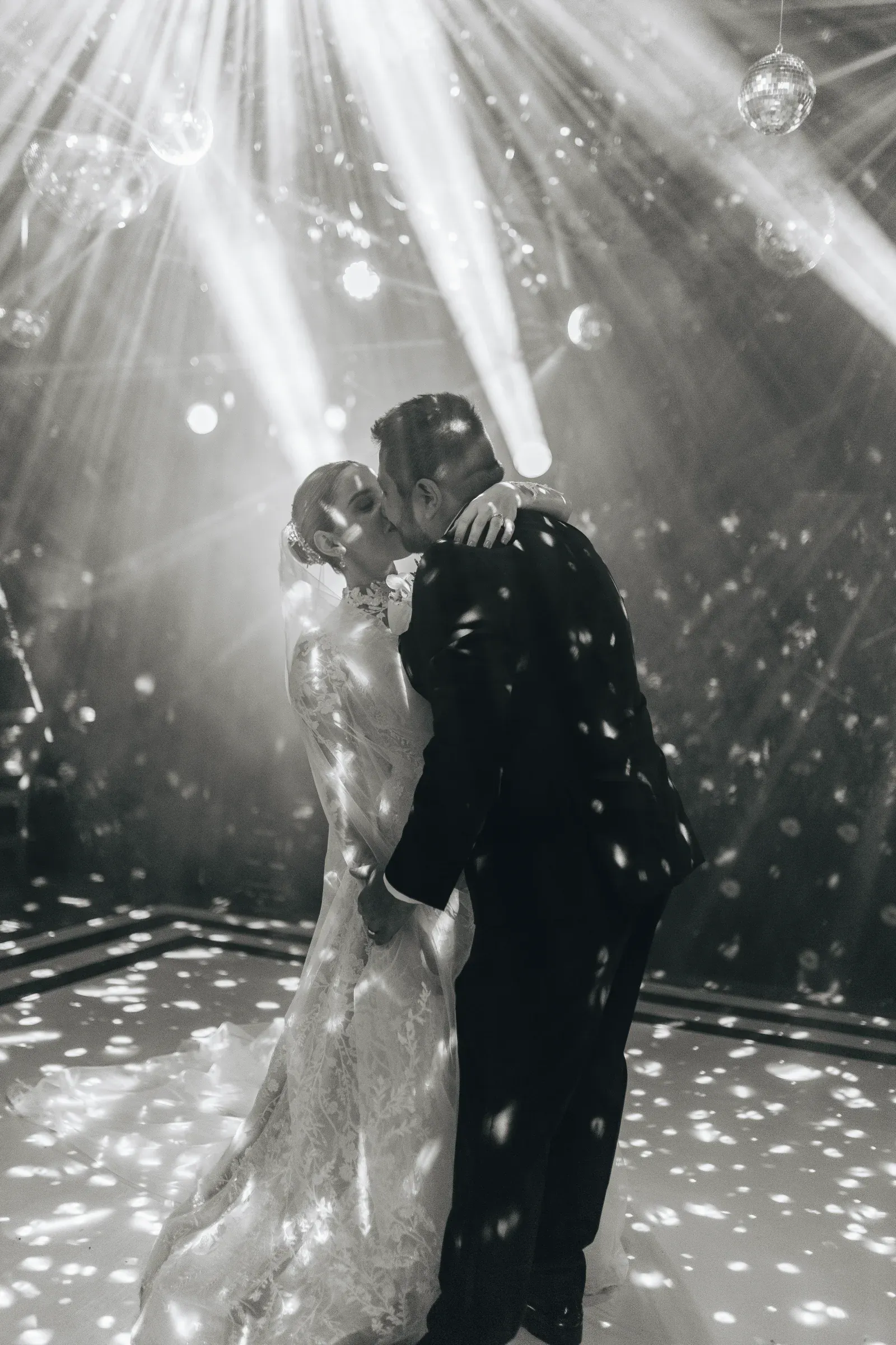 Los novios se dan un beso romántico en la pista de baile. Rodeados de deslumbrantes luces de discoteca y vigas, crean una atmósfera encantadora.