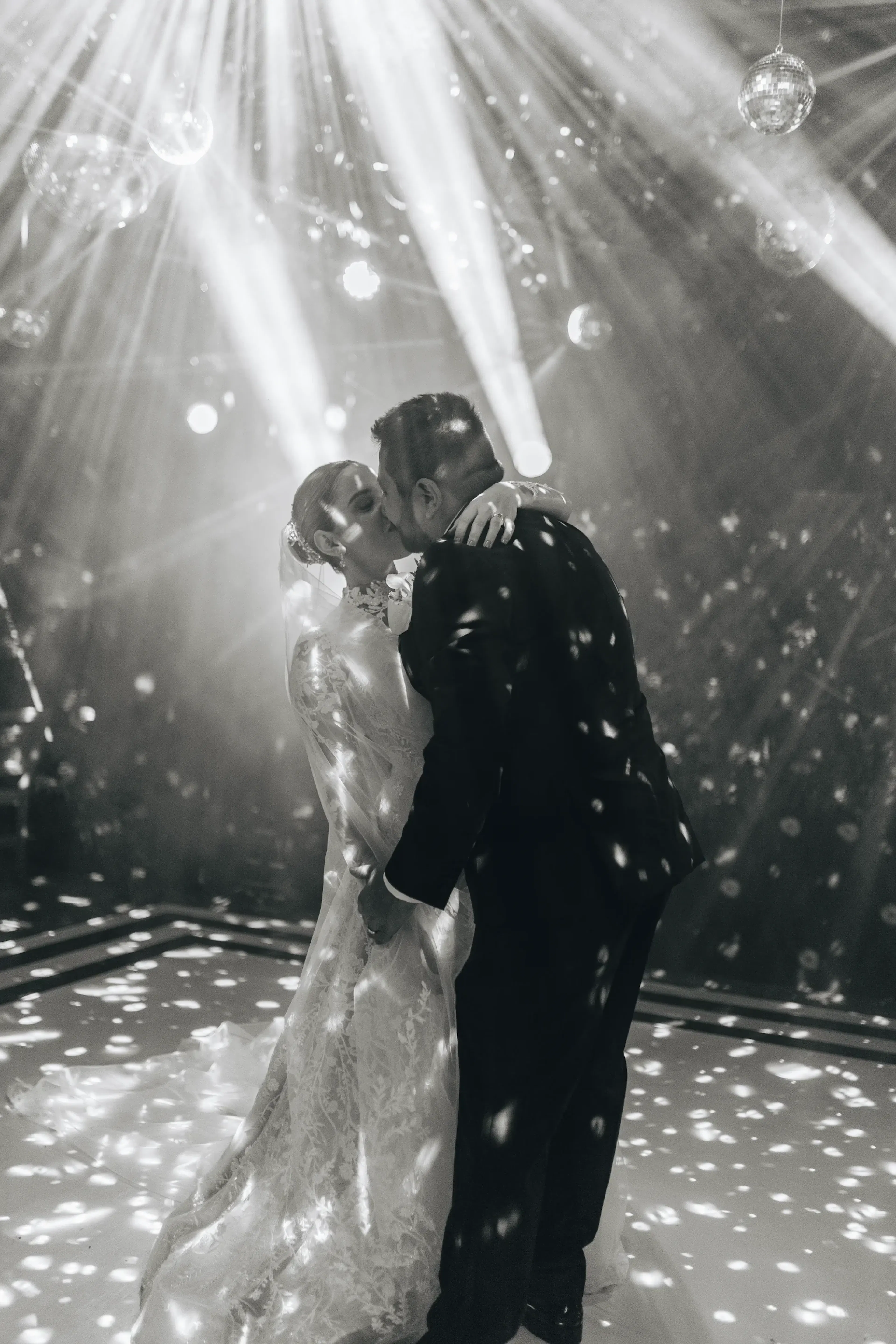 Los novios se dan un beso romántico en la pista de baile. Rodeados de deslumbrantes luces de discoteca y vigas, crean una atmósfera encantadora.