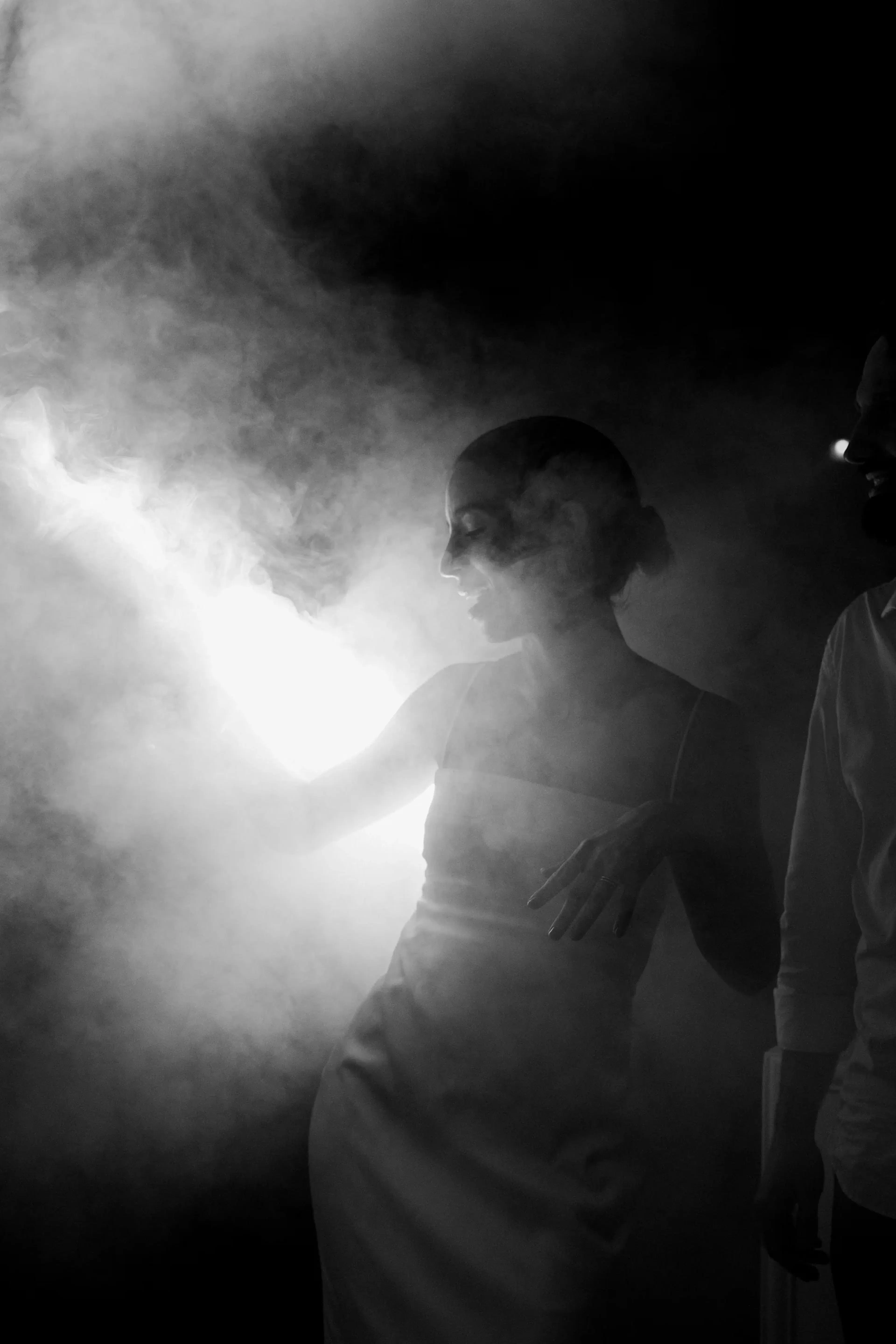 Una mujer con un vestido blanco baila con gracia entre la niebla, iluminada por una luz brillante. La escena es misteriosa y etérea, evocando una atmósfera onírica.