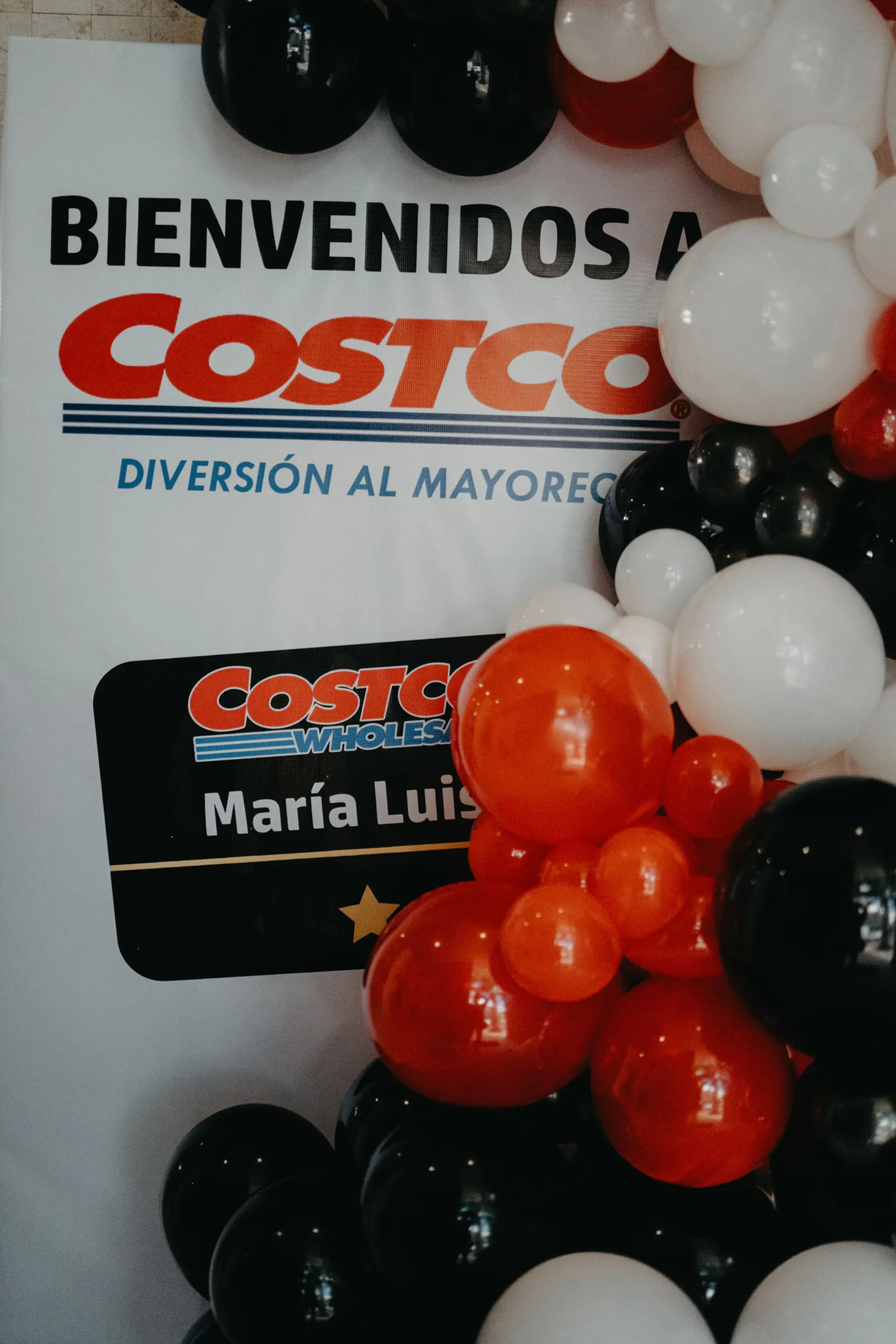 Globos rojos, blancos y negros enmarcan un cartel con "Bienvenidos a Costco" en letras llamativas, creando un ambiente festivo y acogedor.