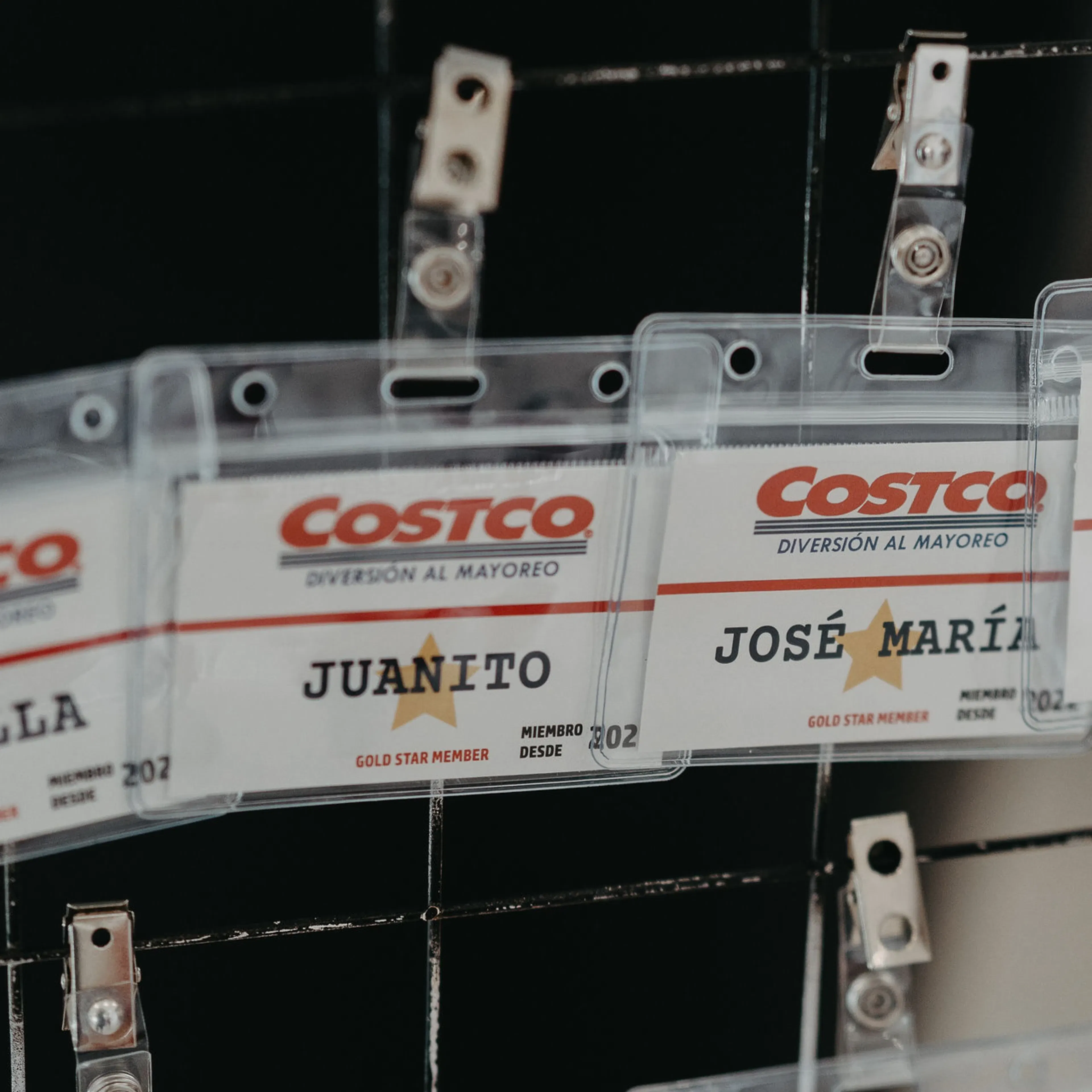 Primer plano de las credenciales de los invitados a la fiesta infantil con temática de Costco sobre una cuadrícula negra. Se ven nombres como Juanito y José María, lo que transmite un ambiente festivo y alegre.