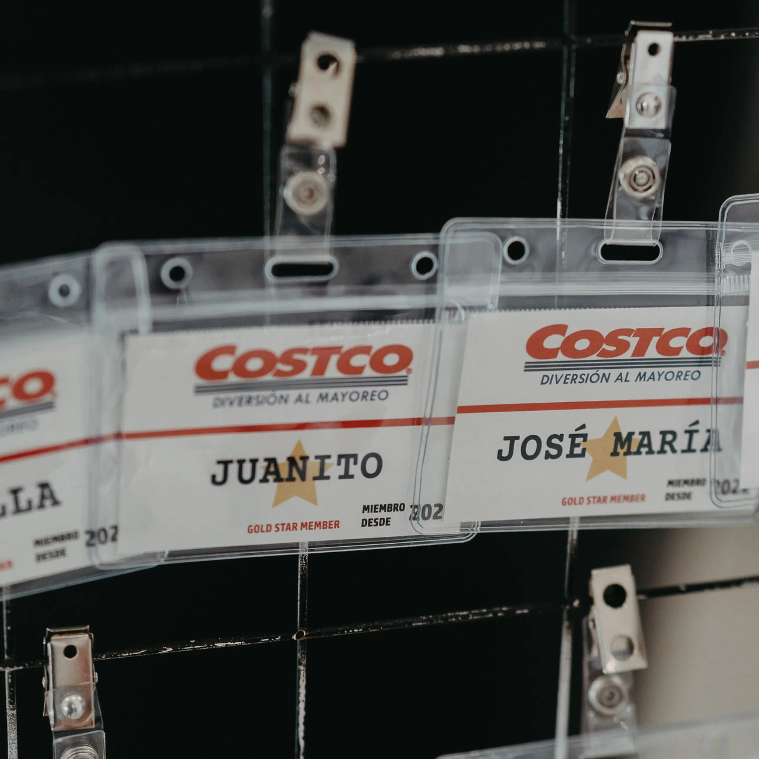 Primer plano de las credenciales de los invitados a la fiesta infantil con temática de Costco sobre una cuadrícula negra. Se ven nombres como Juanito y José María, lo que transmite un ambiente festivo y alegre.
