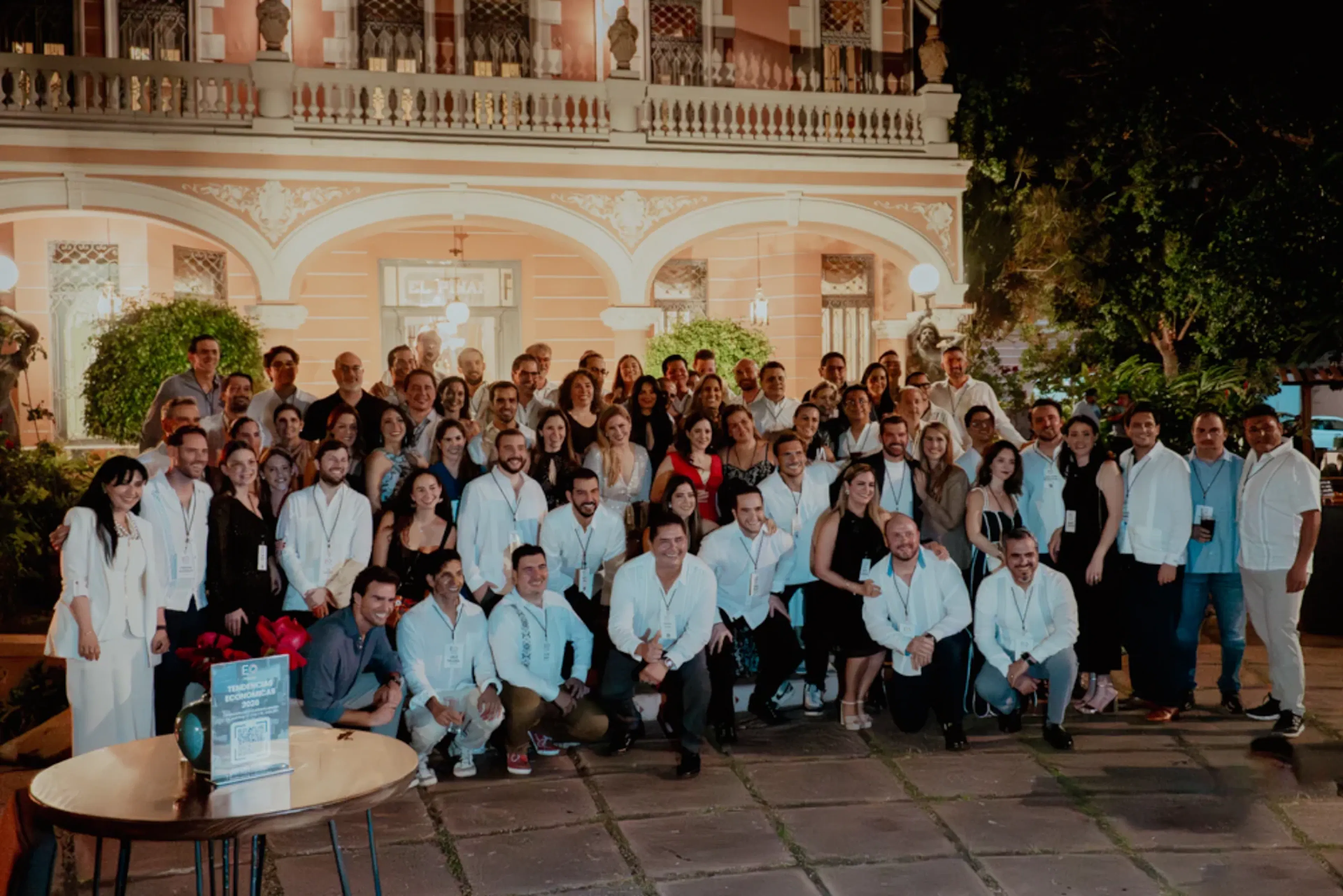 Un grupo numeroso de personas posa junto frente a un imponente edificio histórico por la noche. Parecen estar en un evento formal o de celebración, irradiando alegría y camaradería.