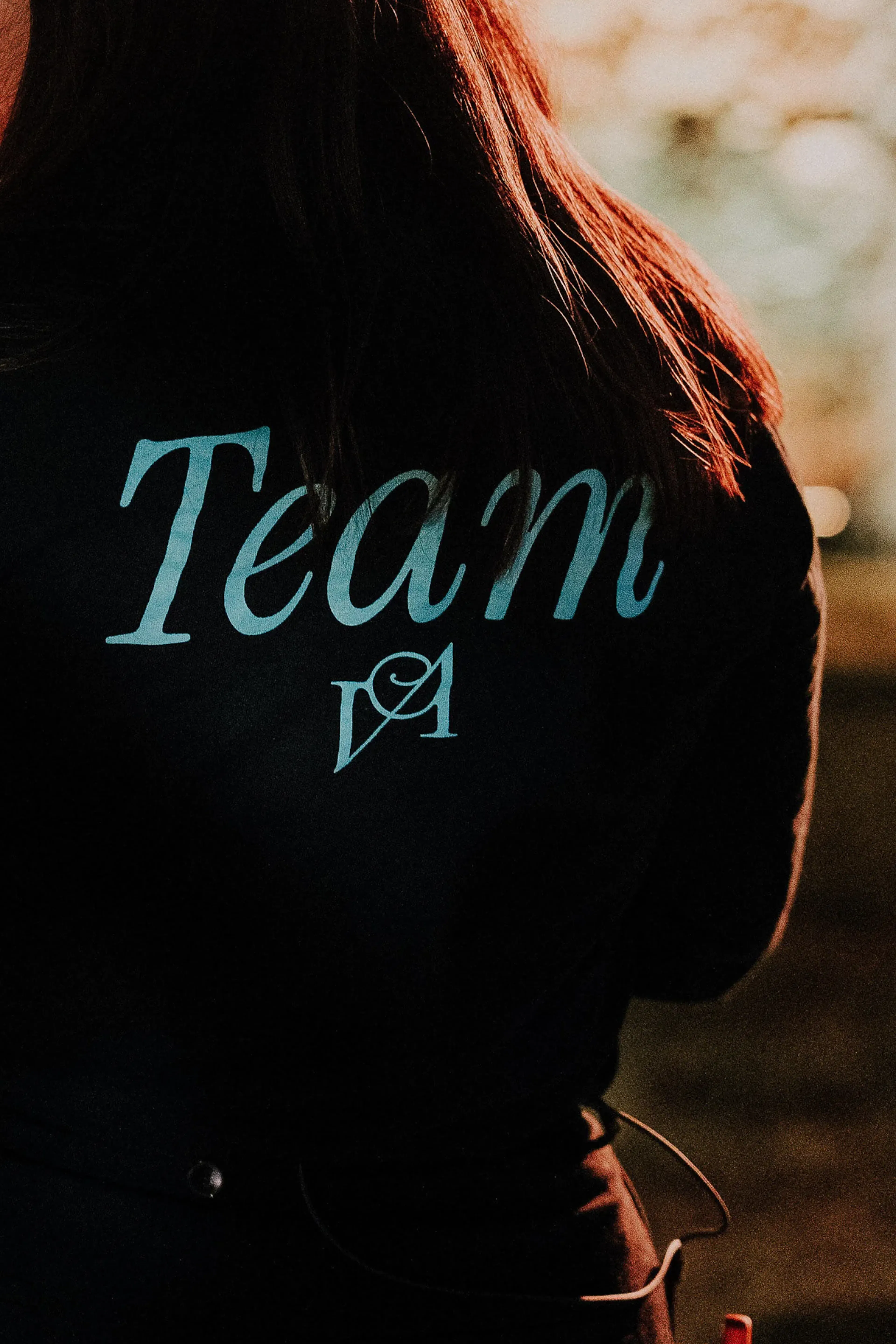 Una persona con una chaqueta oscura del equipo, "Team Vara Alta", parcialmente iluminada, está de espaldas a la cámara. El entorno está tenuemente iluminado, lo que crea un ambiente cálido y concentrado.