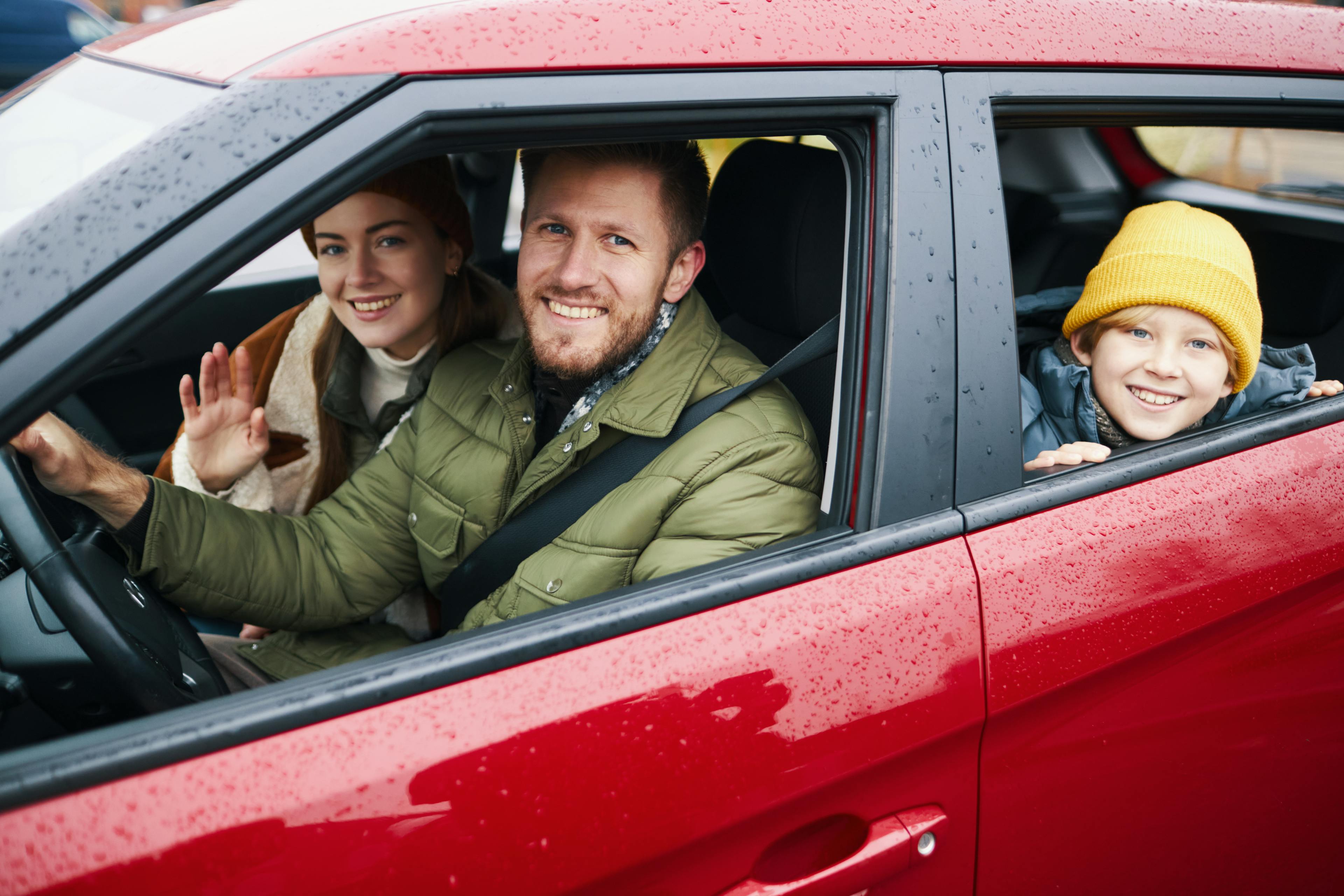 Smiling family enjoying road trip in red car