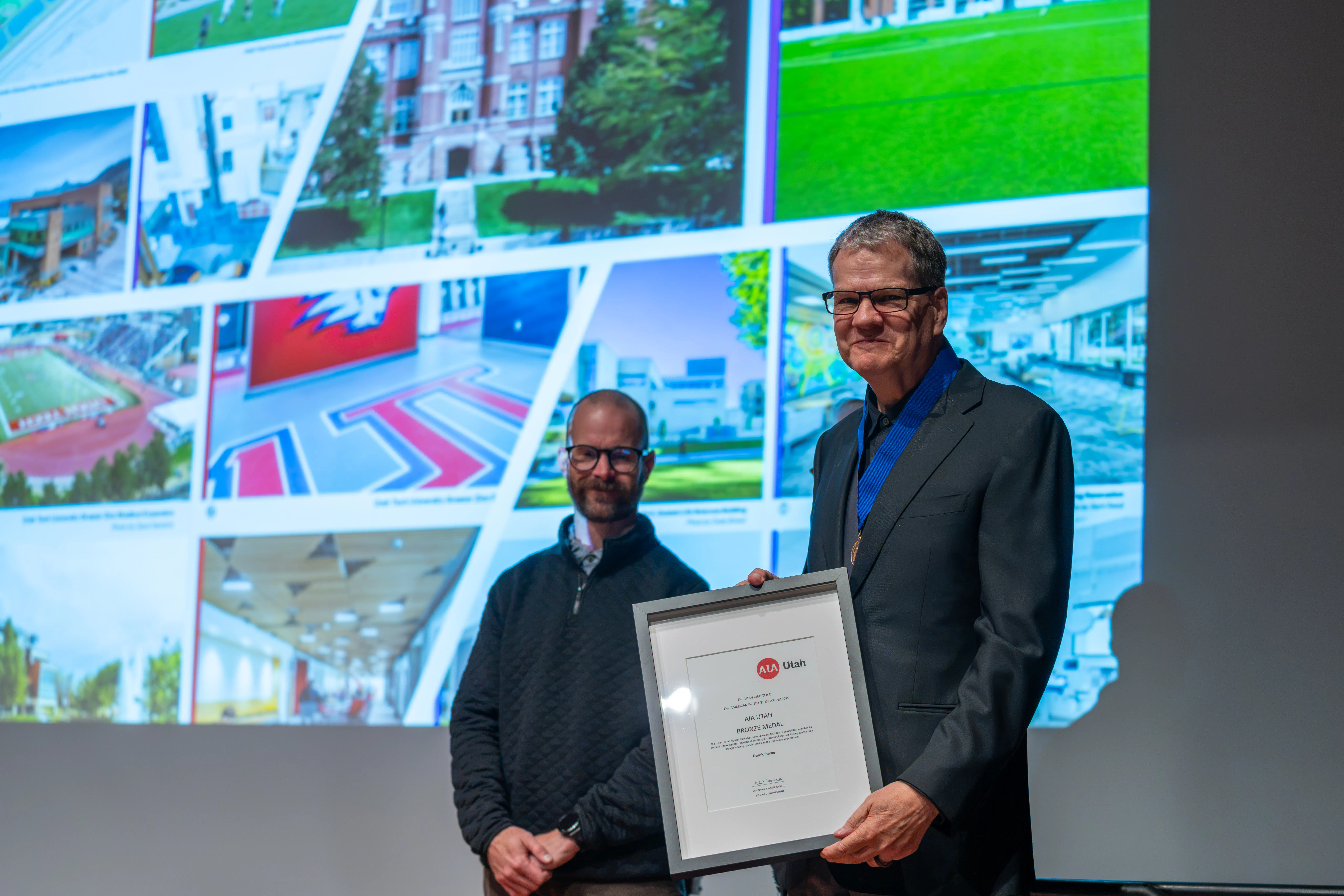 Derek Payne receiving the 2026 AIA Utah Bronze Medal with photos of his projects displayed on a screen in the background.