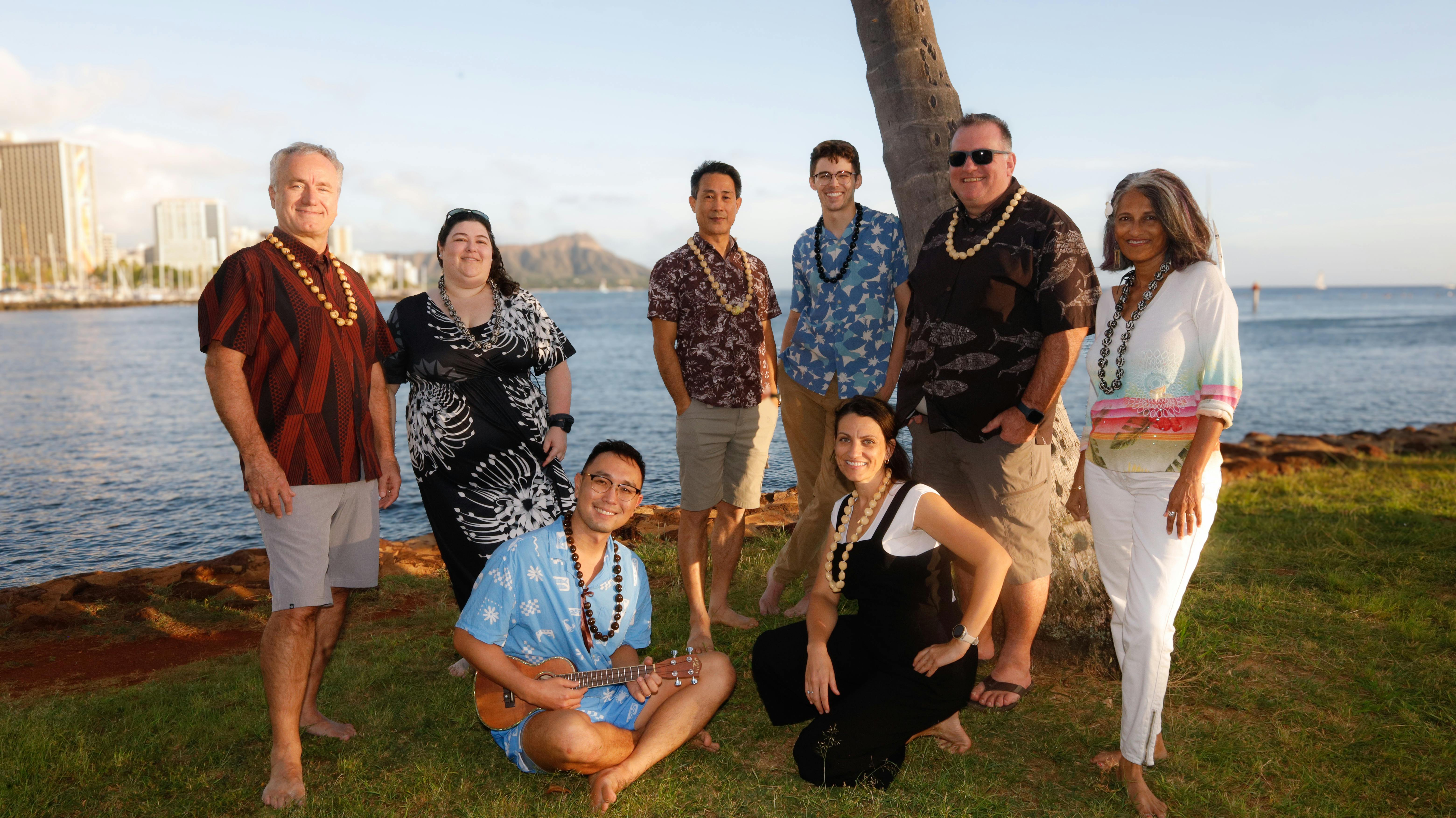 Members of the integrated VCBO–FSC Hawaii team gather by the ocean in aloha attire, with Honolulu’s coastline in the background.
