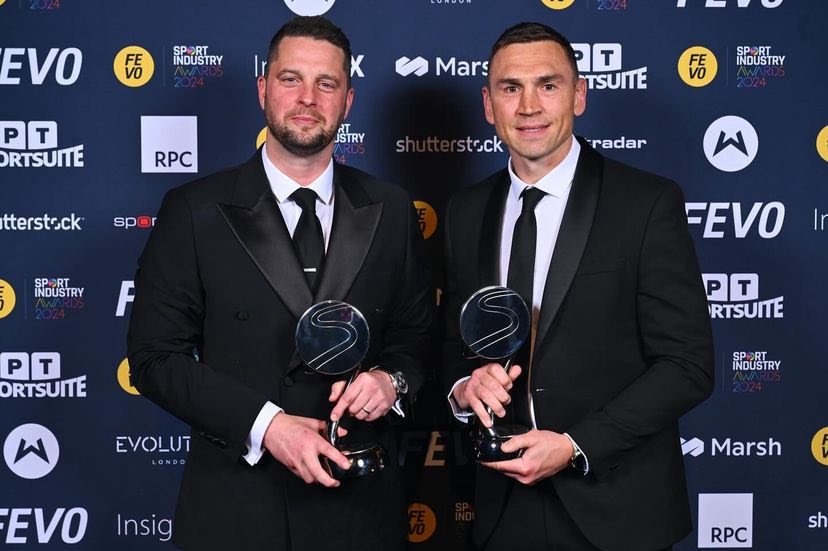 Craig in a dashing suit, holding an award beside his friend.
