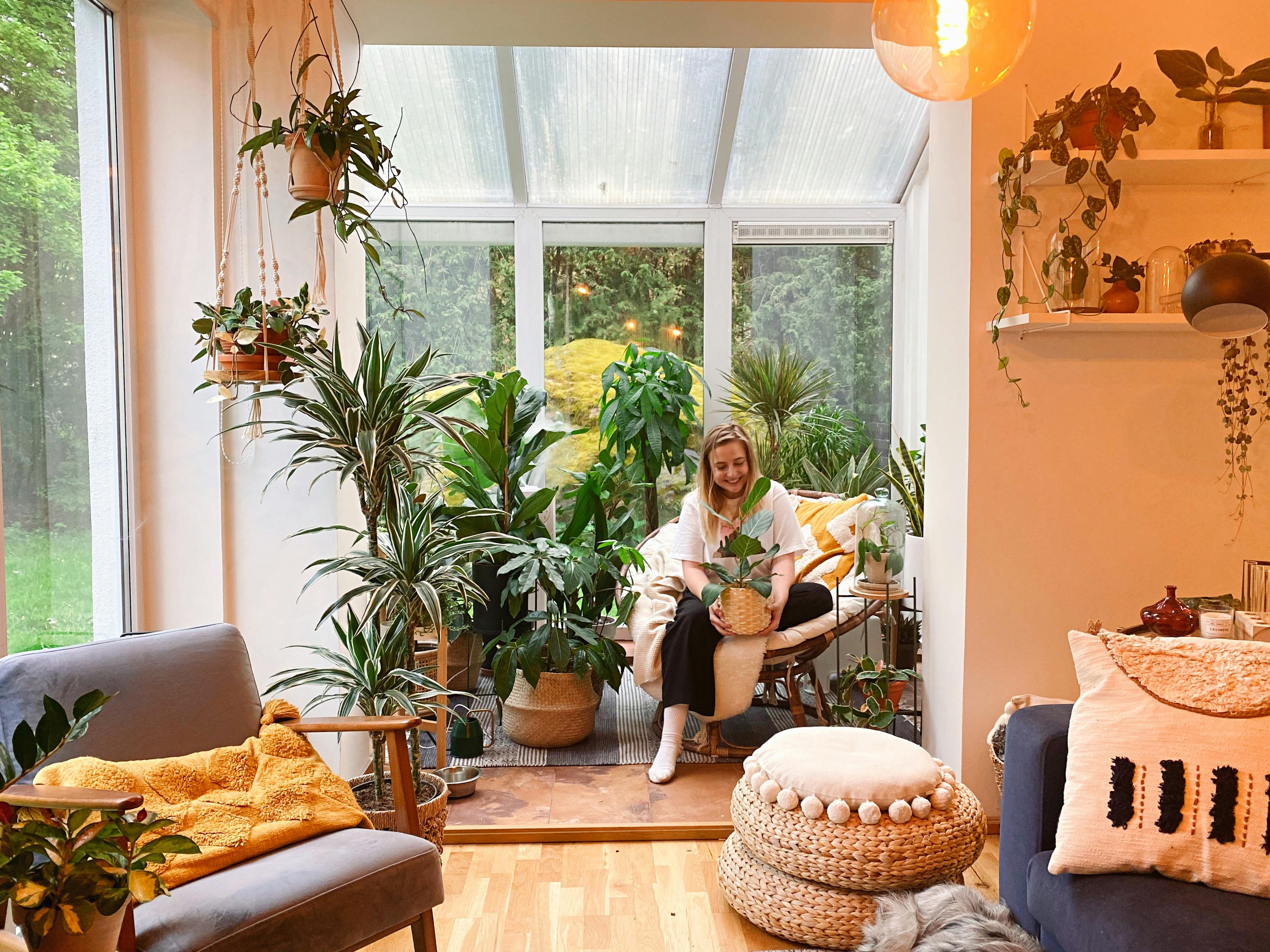 A young lady sat in brightly colored room with potted plants.