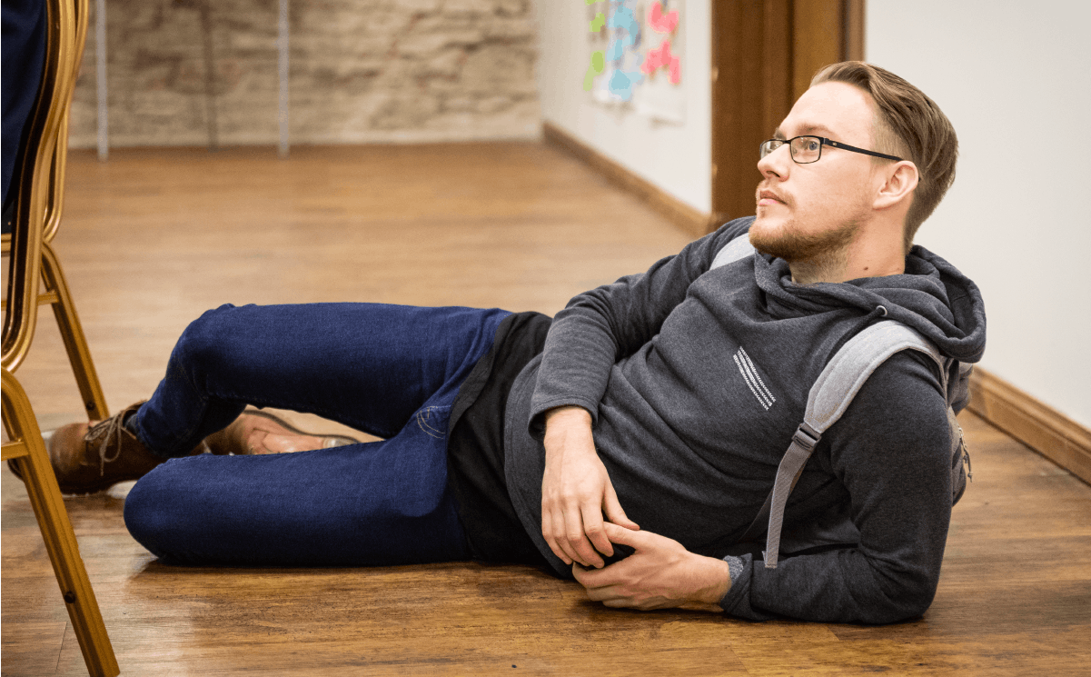A man in blue jeans and a grey hoodie laying down.