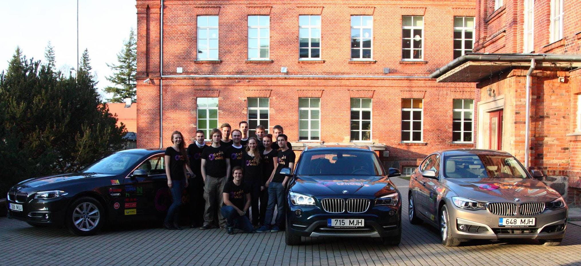 Team stood outside a building with three BMW cars next to them.