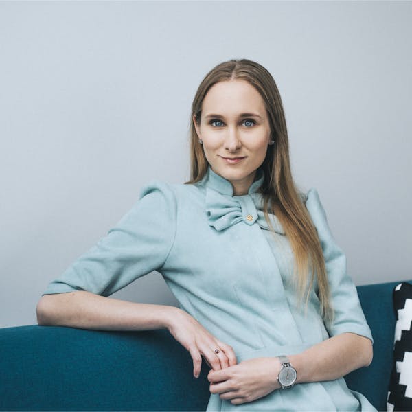 Portrait of Liisi German, a product manager at Veriff, sitting on a blue couch in a light blue dress, looking confident.