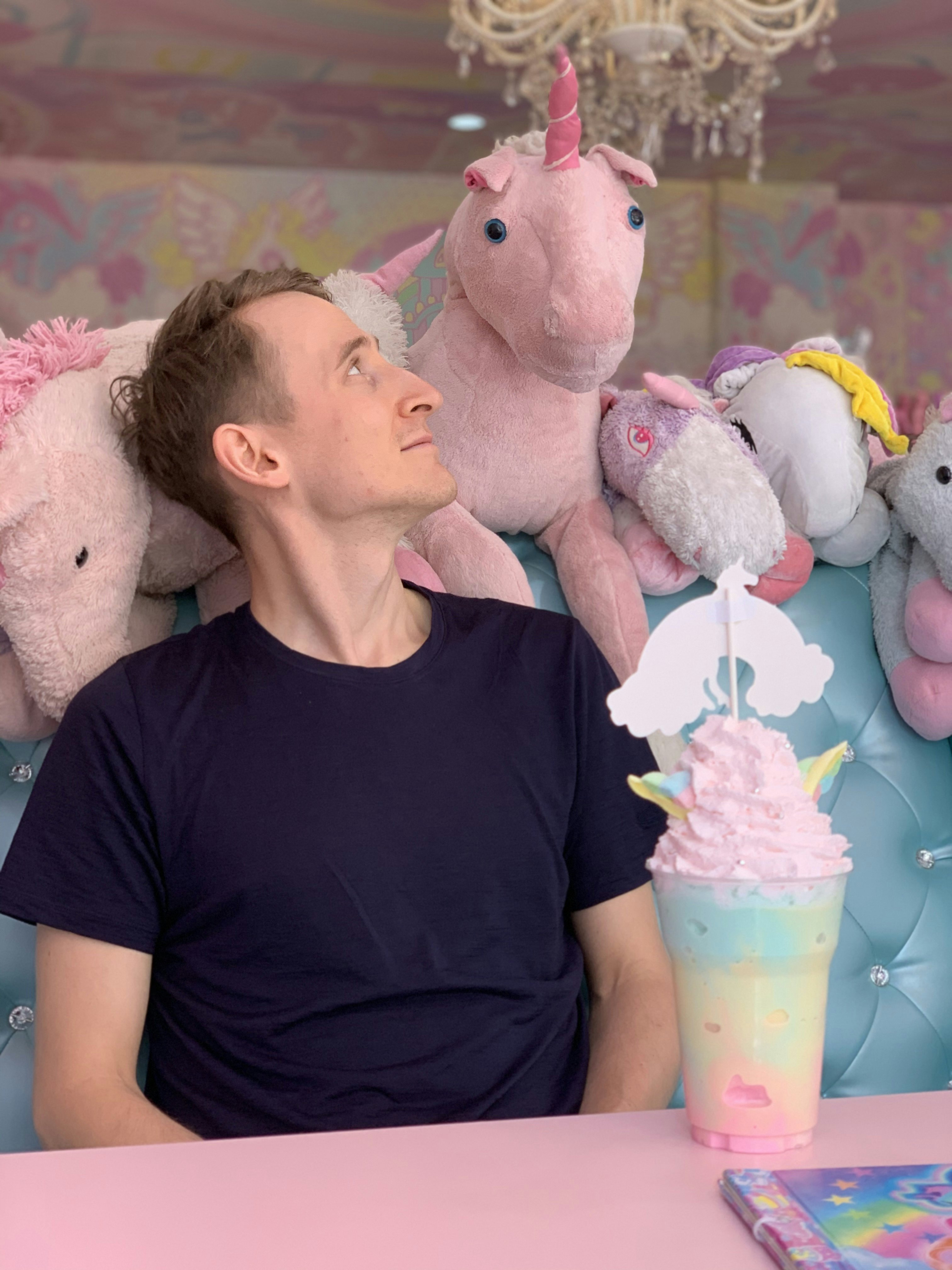 A man in a black t-shirt looking at a pink unicorn