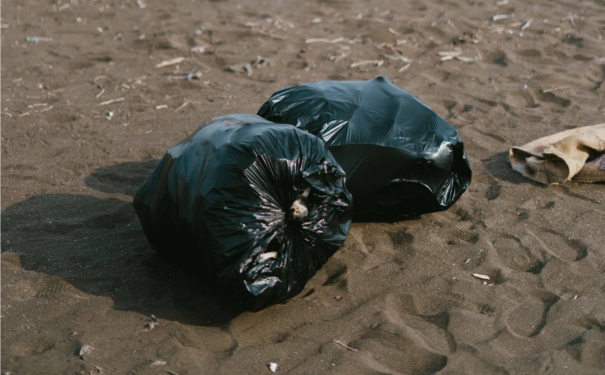 Full black trash bags on sandy beach.