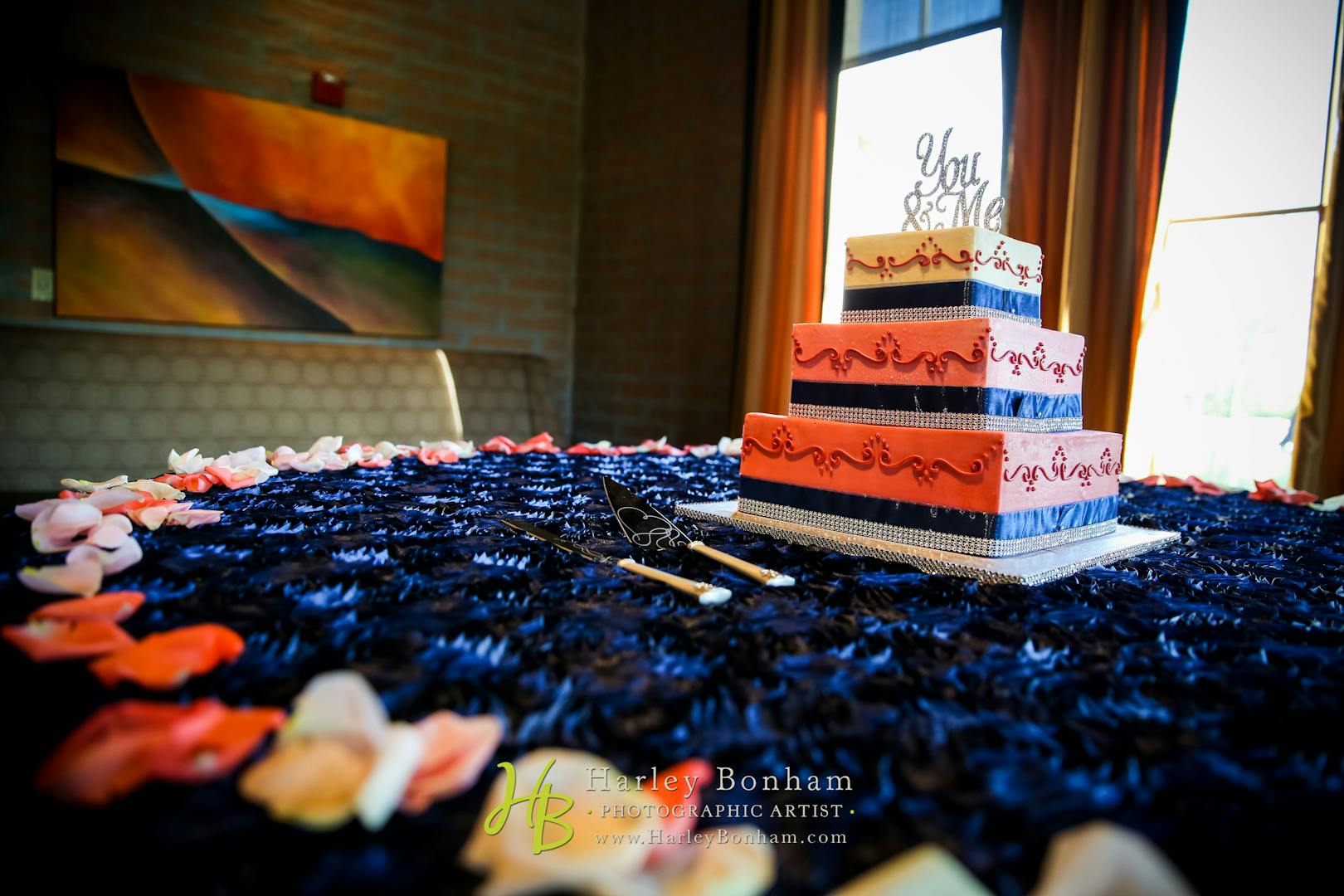 Rose and white wedding cake atop a table adorned with a deep blue cloth and lined with rose petals.