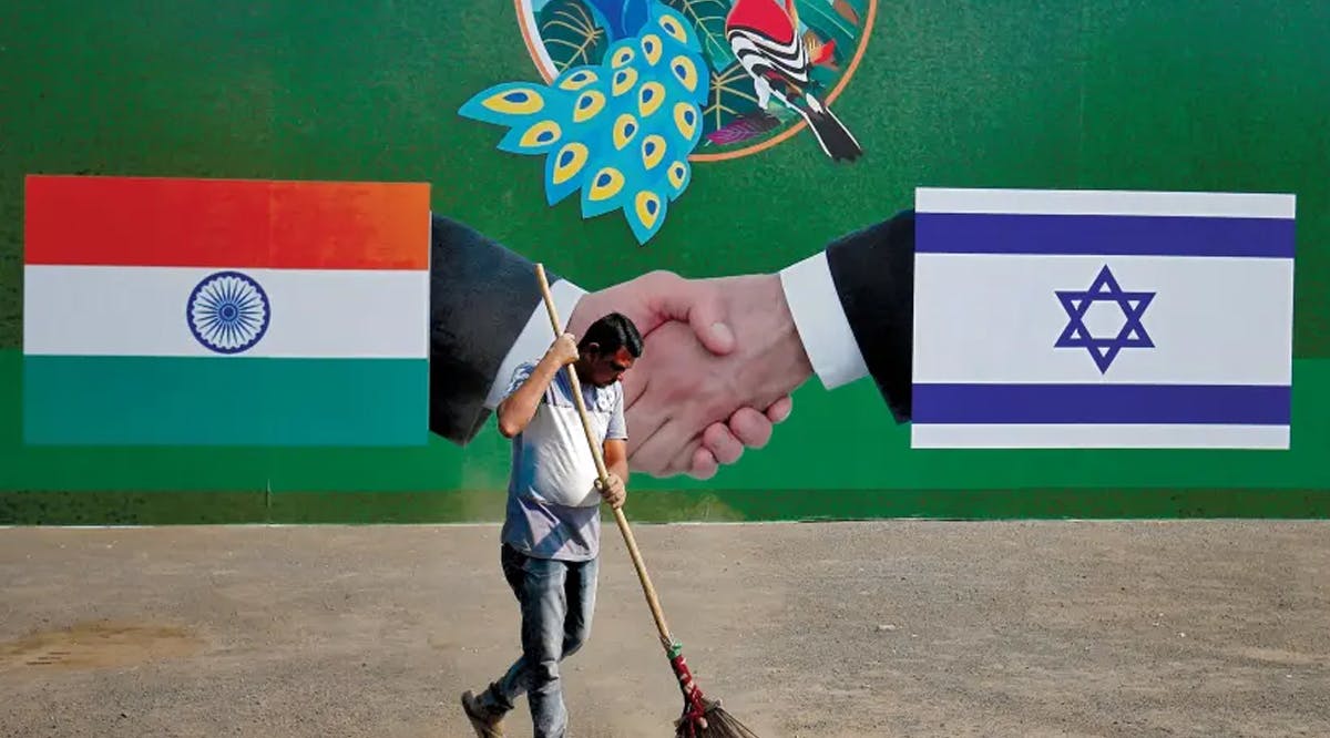 A municipal worker cleans the street in front of a billboard displaying Indian and Israeli flags