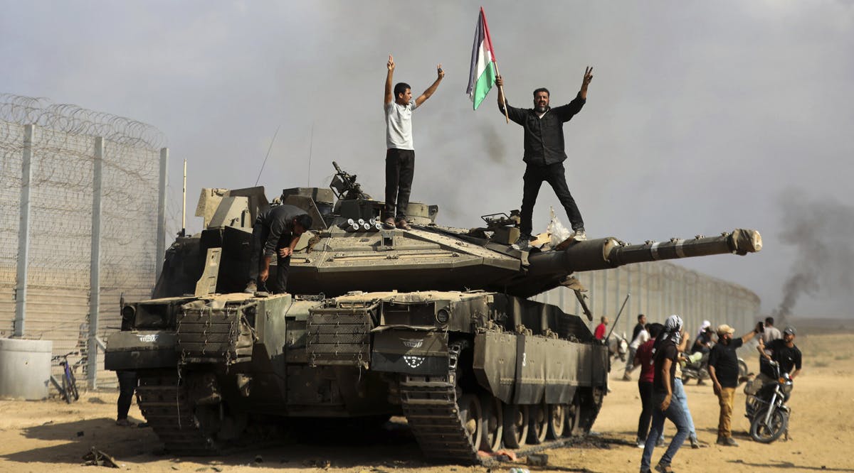 Palestinians wave their national flag and celebrate by a destroyed Israeli tank at the Gaza Strip fence east of Khan Younis