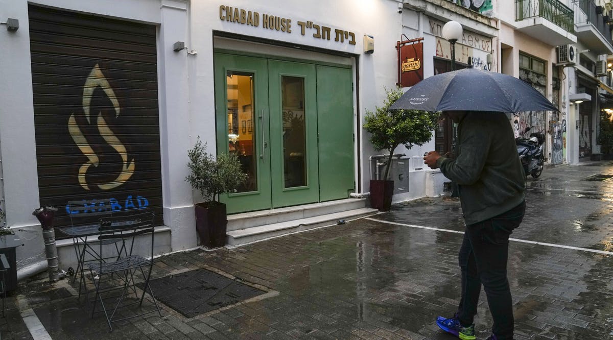 A man holding an umbrella stands in front of a Jewish center that Greek officials believe was one of the targets of a planned terrorist attack, in central Athens