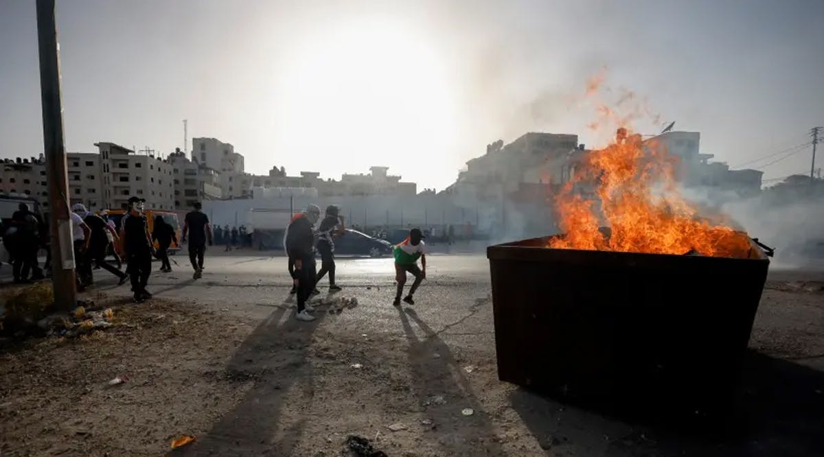 People are pictured next to a fire burning in a large container as Palestinians clash with Israeli forces during a protest over tensions in Jerusalem's Al-Aqsa Mosque