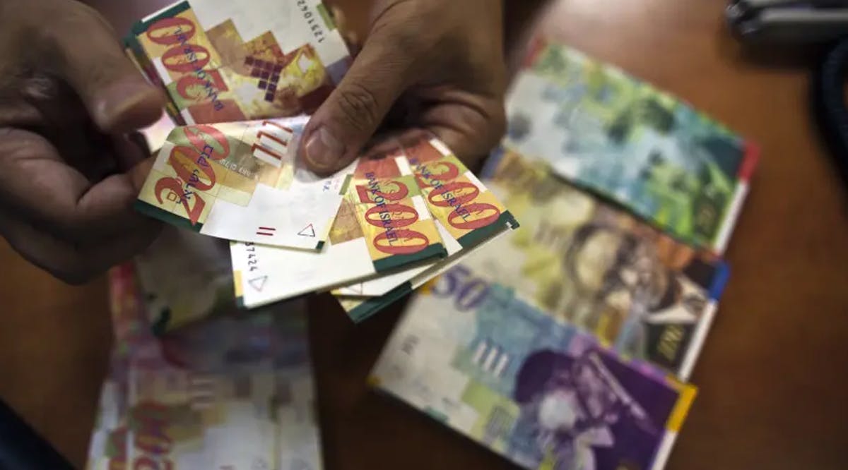 A bank employee counts Israeli Shekel notes for the camera at a bank branch in Tel Aviv