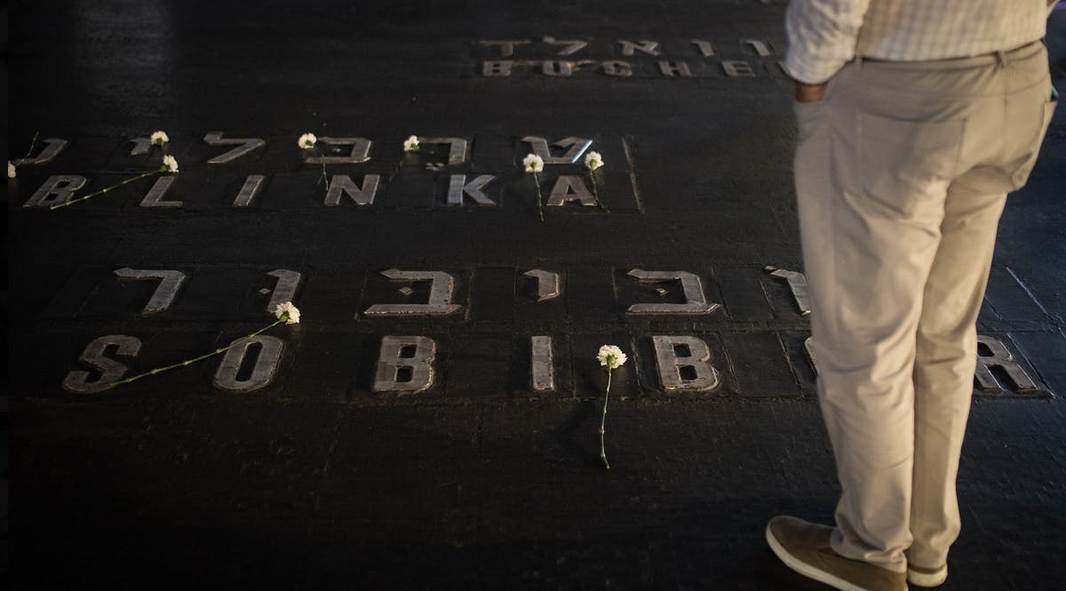 Relatives and friends of Holocaust survivors place flowers on names of concentration camps seen on the floor of the Hall of Remembrance at Yad Vashem