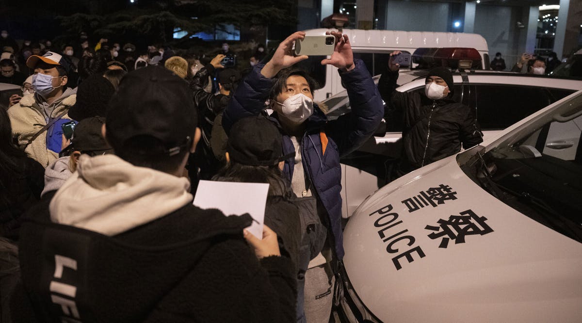 Protesters against China's strict COVID rules pass near a police car in Beijing