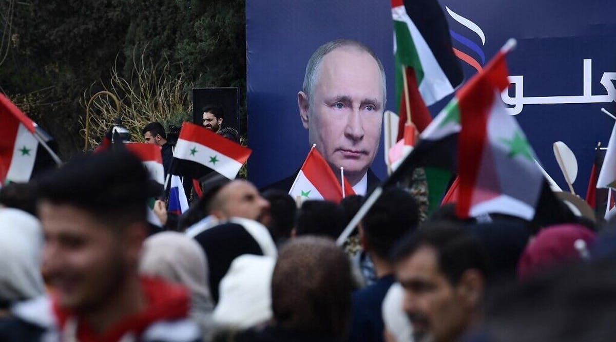 Syrian students wave the Syrian, Russian and Palestinian flags under a billboard bearing the portrait of Russian President Vladimir Putin during a demonstration in support of Russia