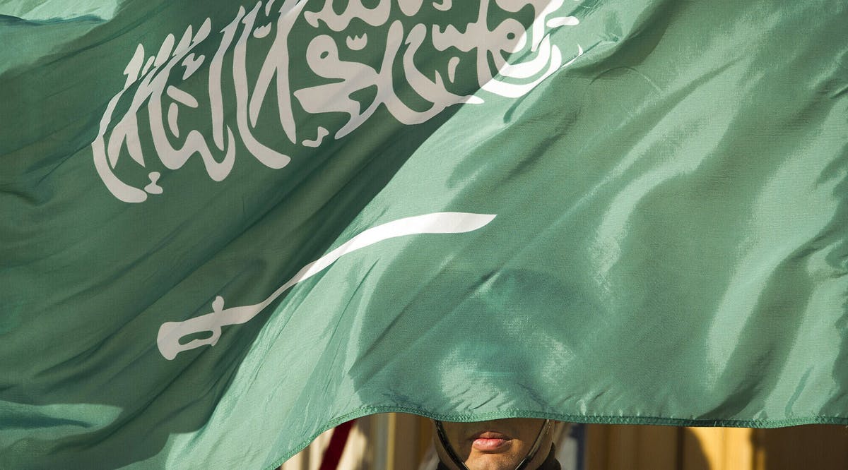 An honor guard member is covered by the flag of Saudi Arabia