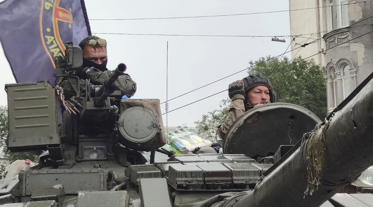 Servicemen sit in a tank with a flag of the Wagner Group military company