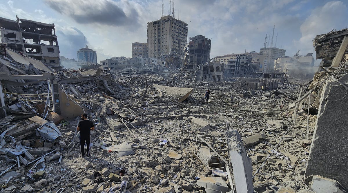 Palestinians walk through the rubble of buildings destroyed by Israeli airstrikes in Gaza City