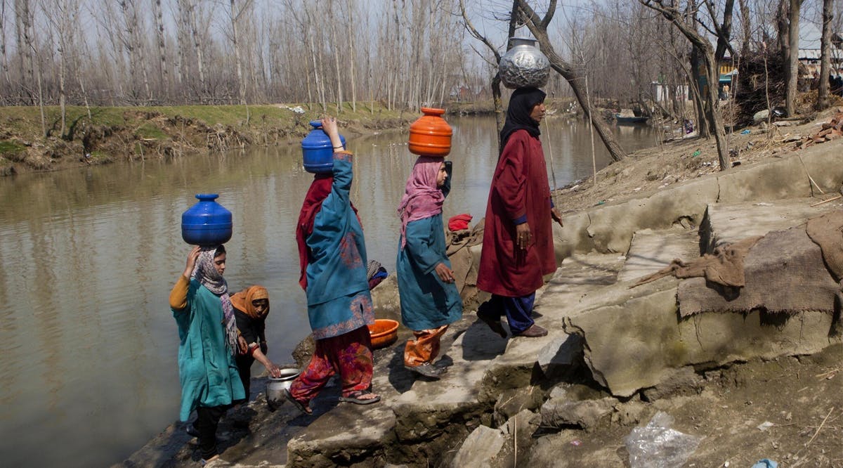 Kashmiri village women carry vessels containing water after filling them from a polluted river