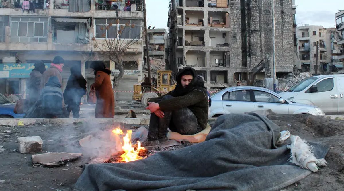 A man who evacuated his home warms up next to a fire on a street, in the aftermath of the earthquake, in Aleppo, Syria