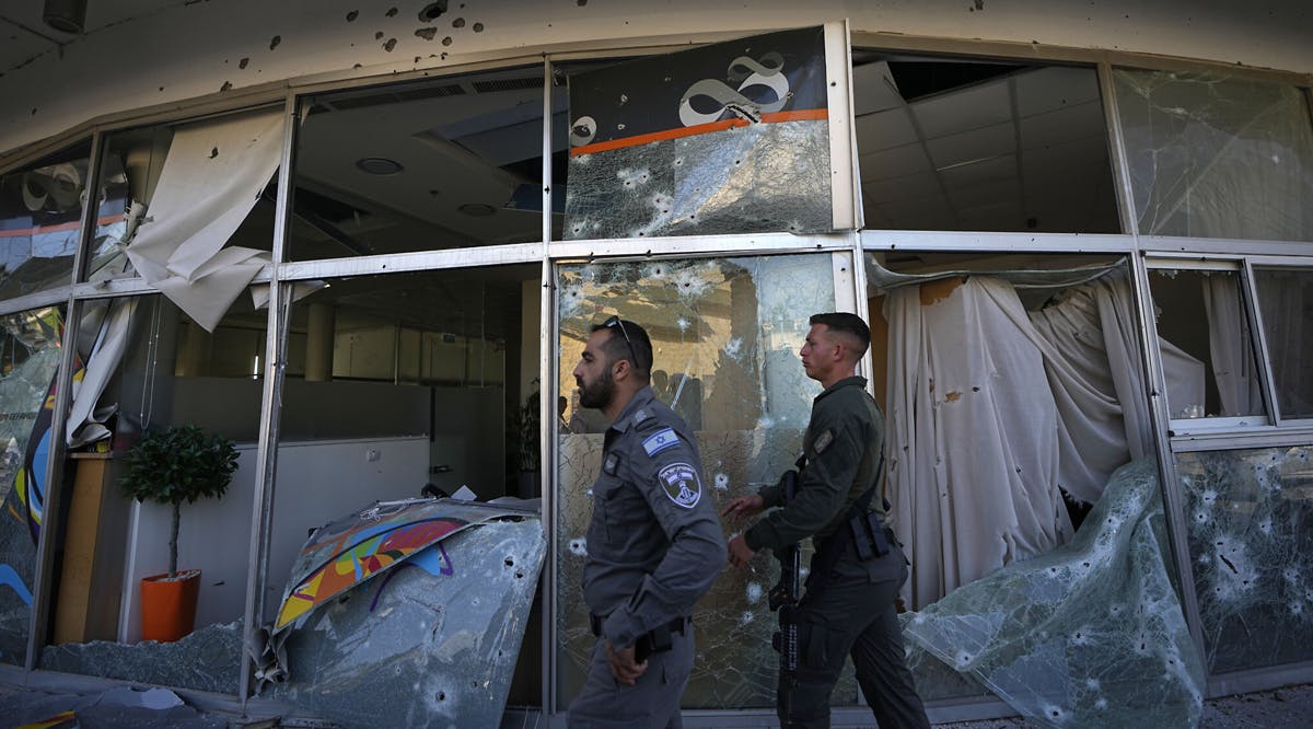 Israeli security forces walk next to a bank damaged by an intercepted rocket fired from Lebanon