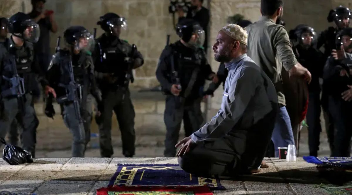 A Palestinian man prays as Israeli police gather during clashes at the compound that houses Al-Aqsa Mosque