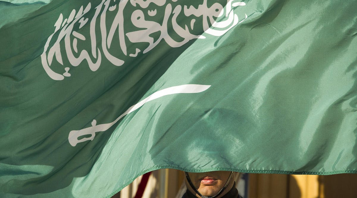 An honor guard member is covered by the flag of Saudi Arabia