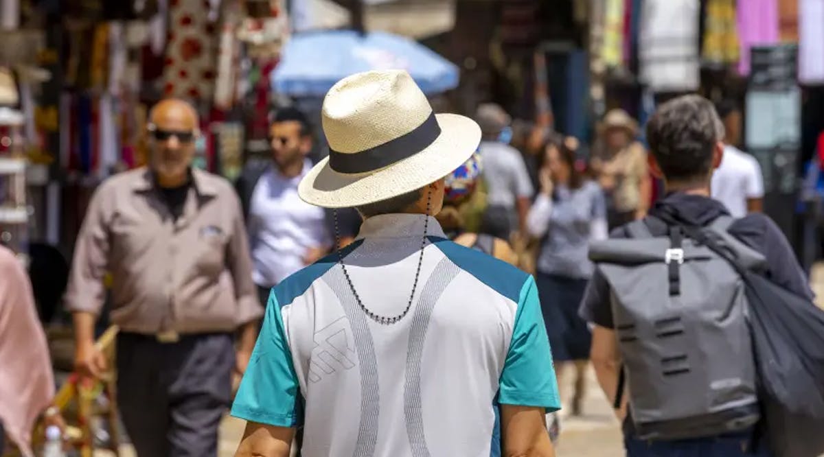 A man wearing a hat during a hot sunny summer day walks near the Tower of David in Jerusalem Old City