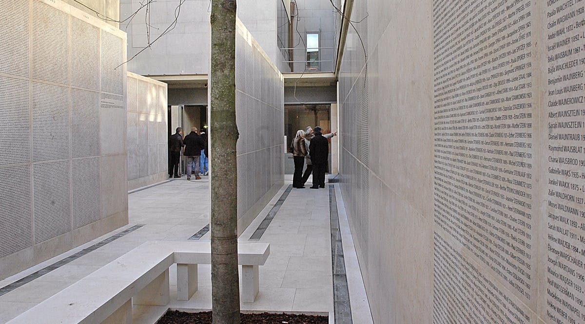 A view of pale stone walls engraved with the names of 76,000 people deported from France to Nazi death camps during World War II
