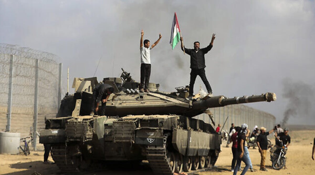 Gazans celebrate by a destroyed Israeli tank at the broken Israel-Gaza border fence, east of Khan Younis