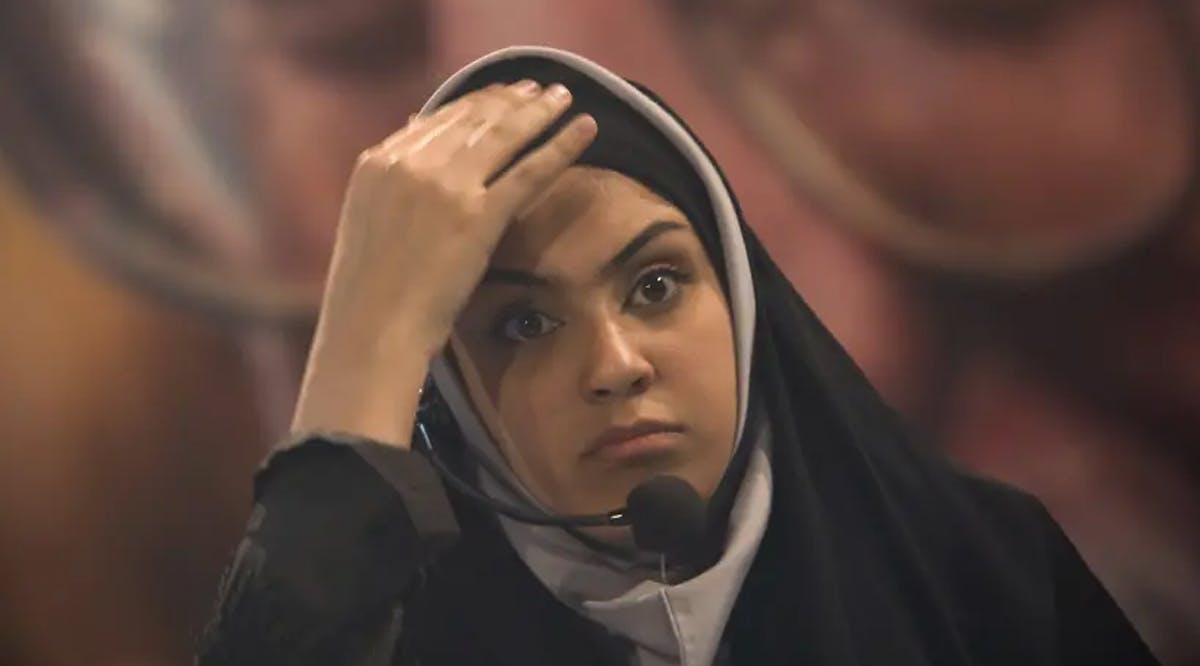 An Iranian woman adjusts her hijab as she stands in front of a portrait of Iran's Supreme Leader Ayatollah Ali Khamenei