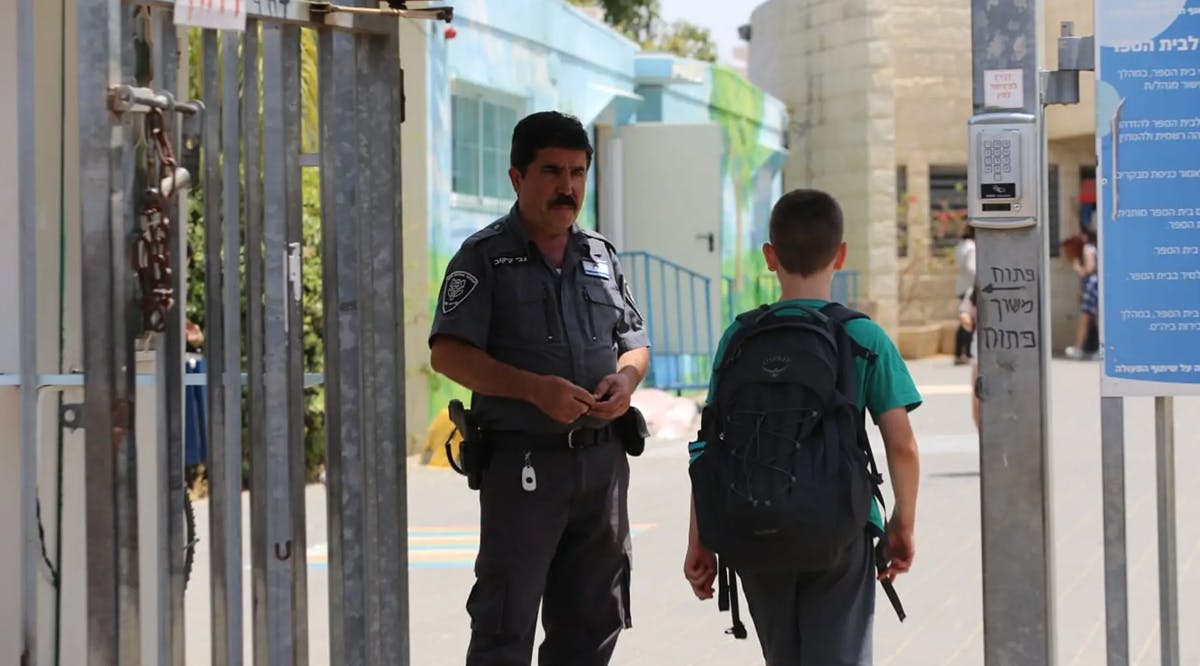 An Israeli school security officer watches on as students enter school