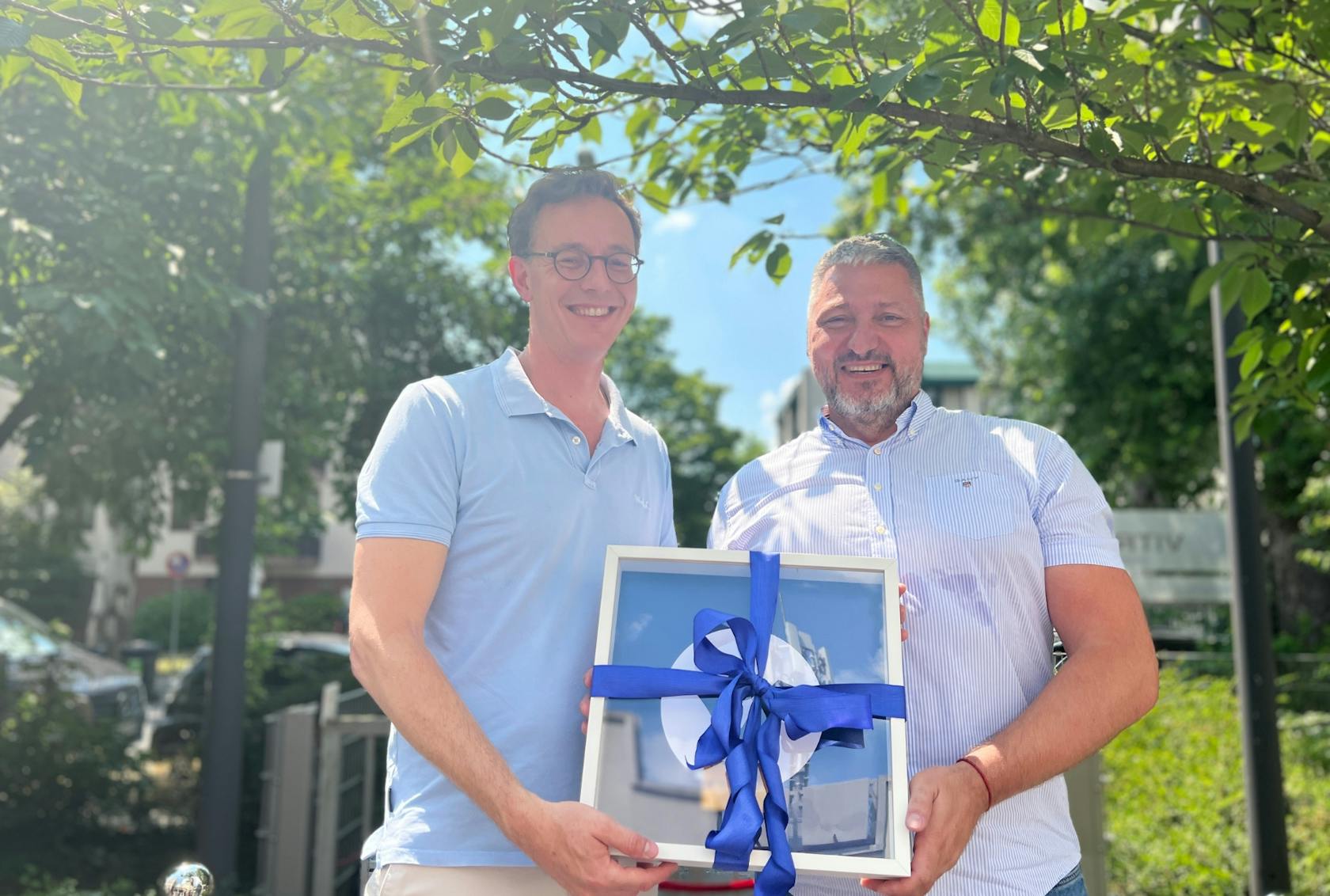 Daniel Scholz-Stein and Matej Okali handing over a gift in the sunshine.