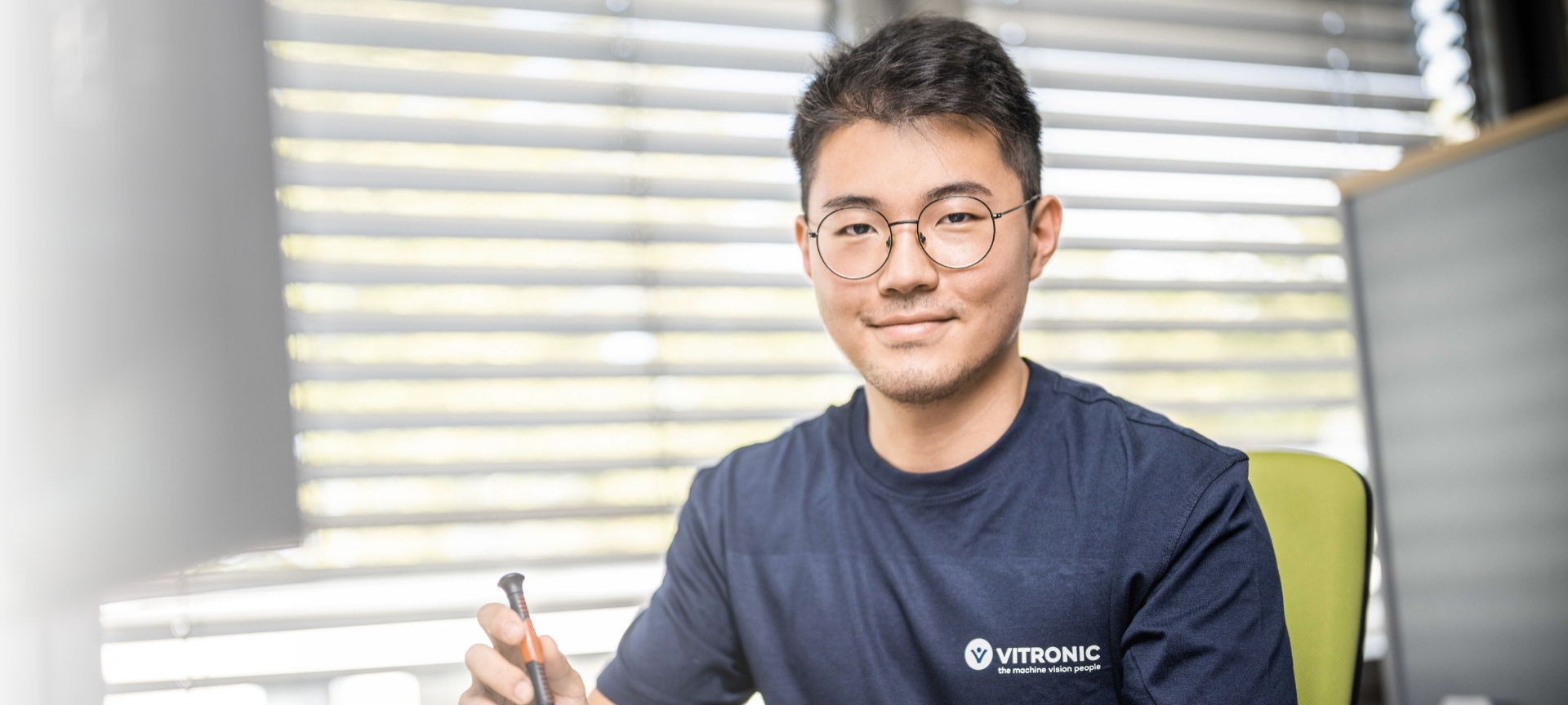 Young trainee at VITRONIC sitting at a desk working on hardware components of an image processing system.