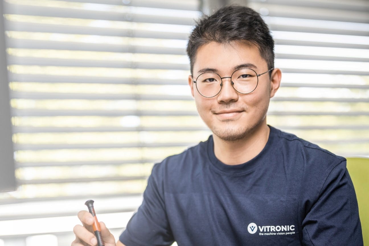 Young trainee at VITRONIC sitting at a desk working on hardware components of an image processing system.