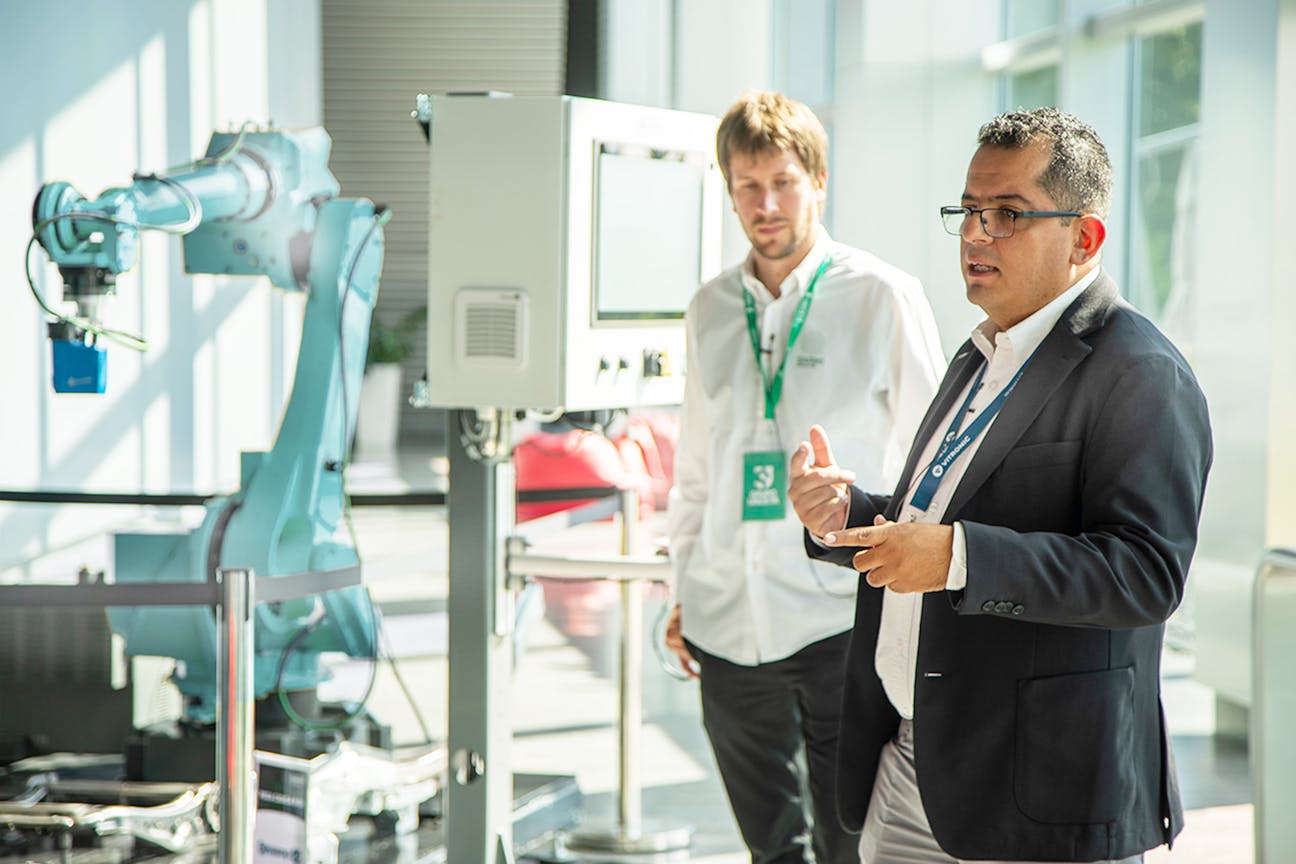VITRONIC employee stands in front of a robot to demonstrate weld seam inspection and explains the process to the audience.