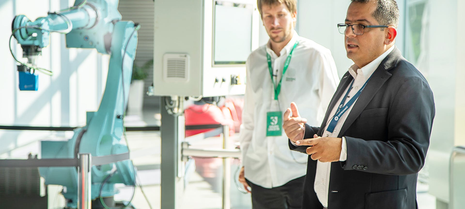 VITRONIC employee stands in front of a robot to demonstrate weld seam inspection and explains the process to the audience.