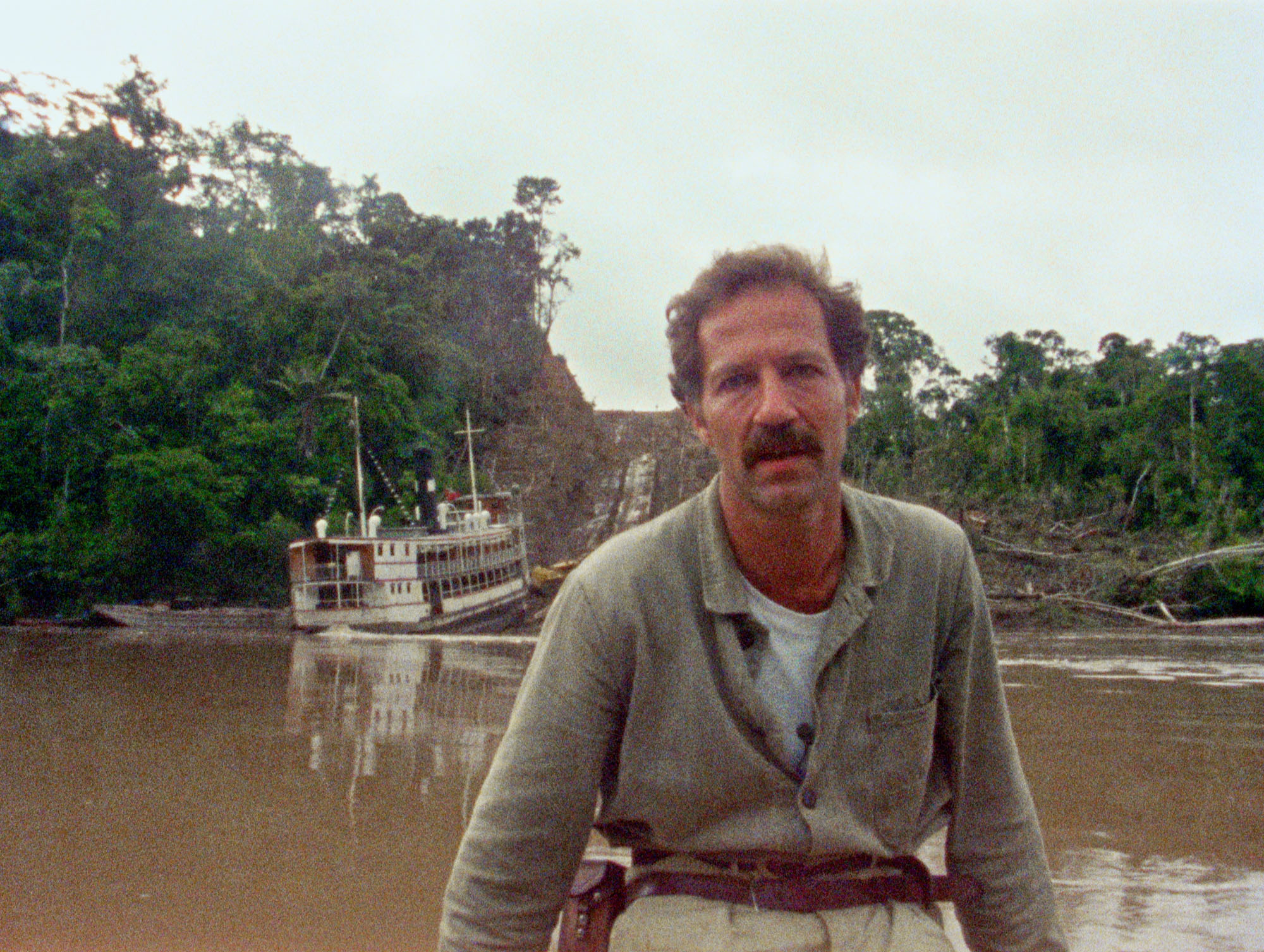 Man sits looking into the camera by a river