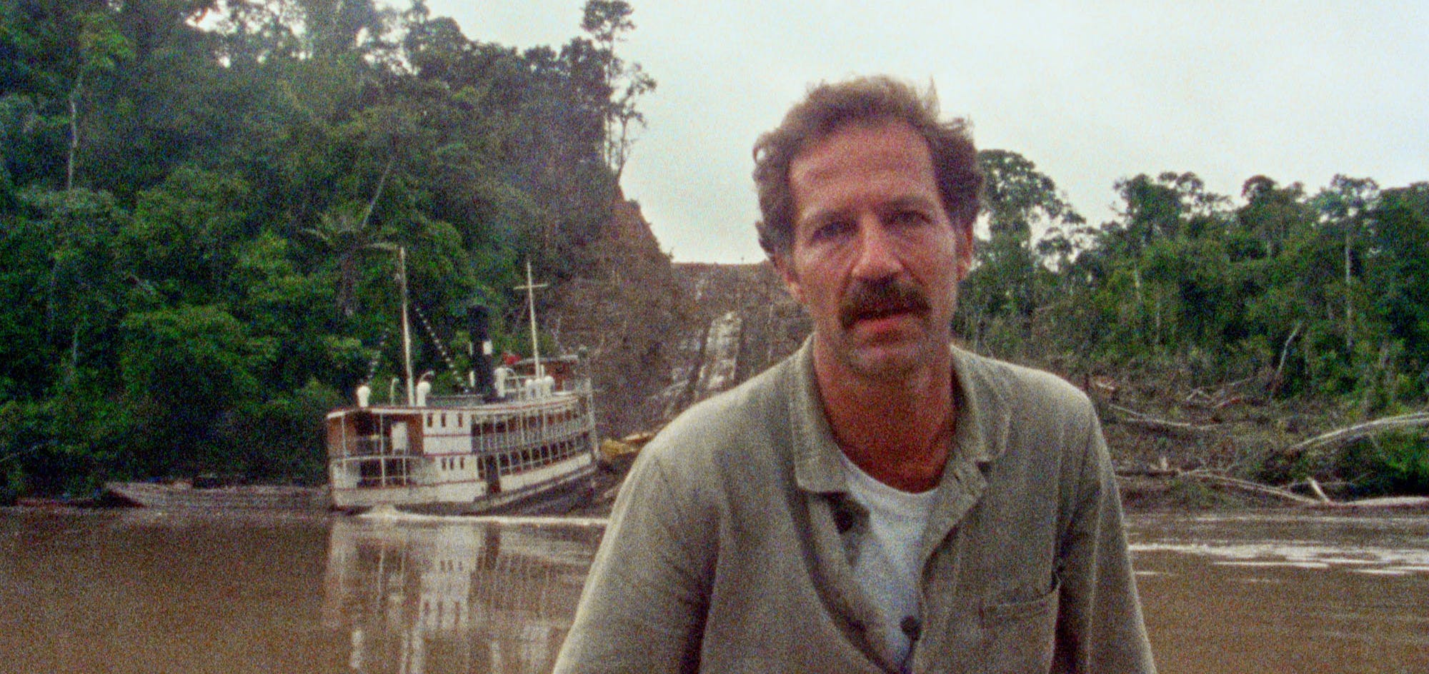 Man sits looking into the camera by a river