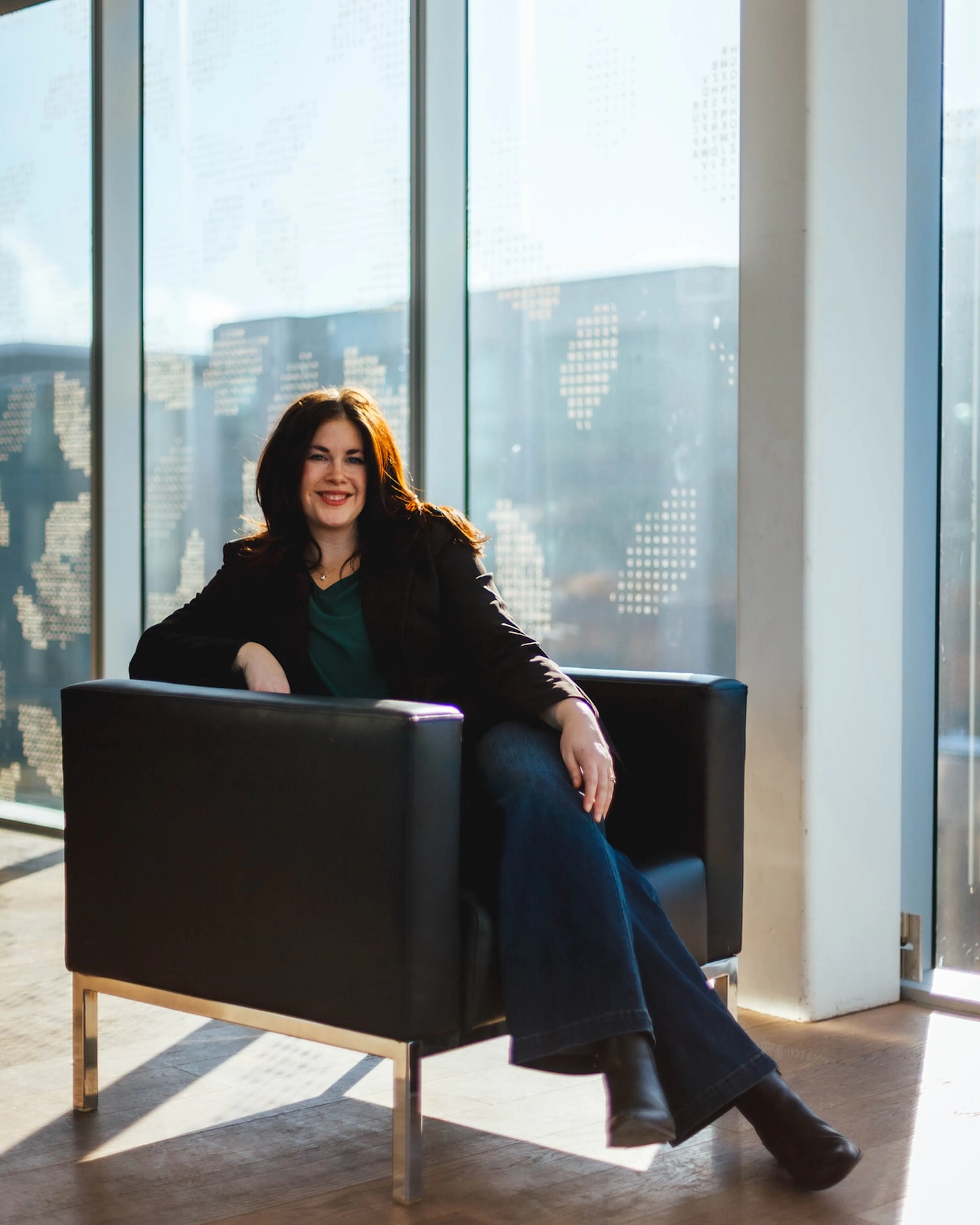 Natasha smiling sitting in an armchair in a bright window
